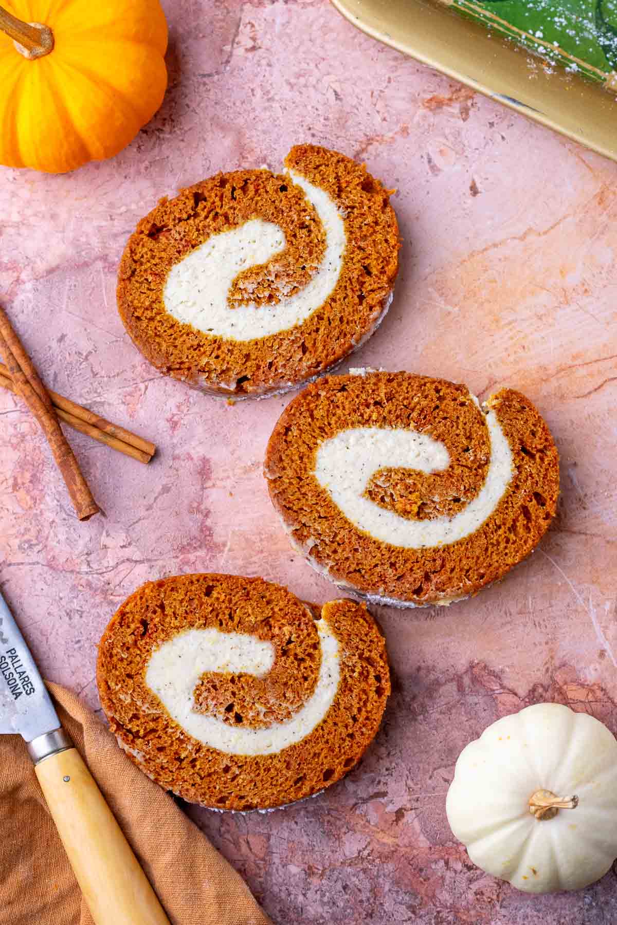 Three slices of sourdough pumpkin roll with brown butter cream cheese surrounded by pumpkins and cinnamon sticks.