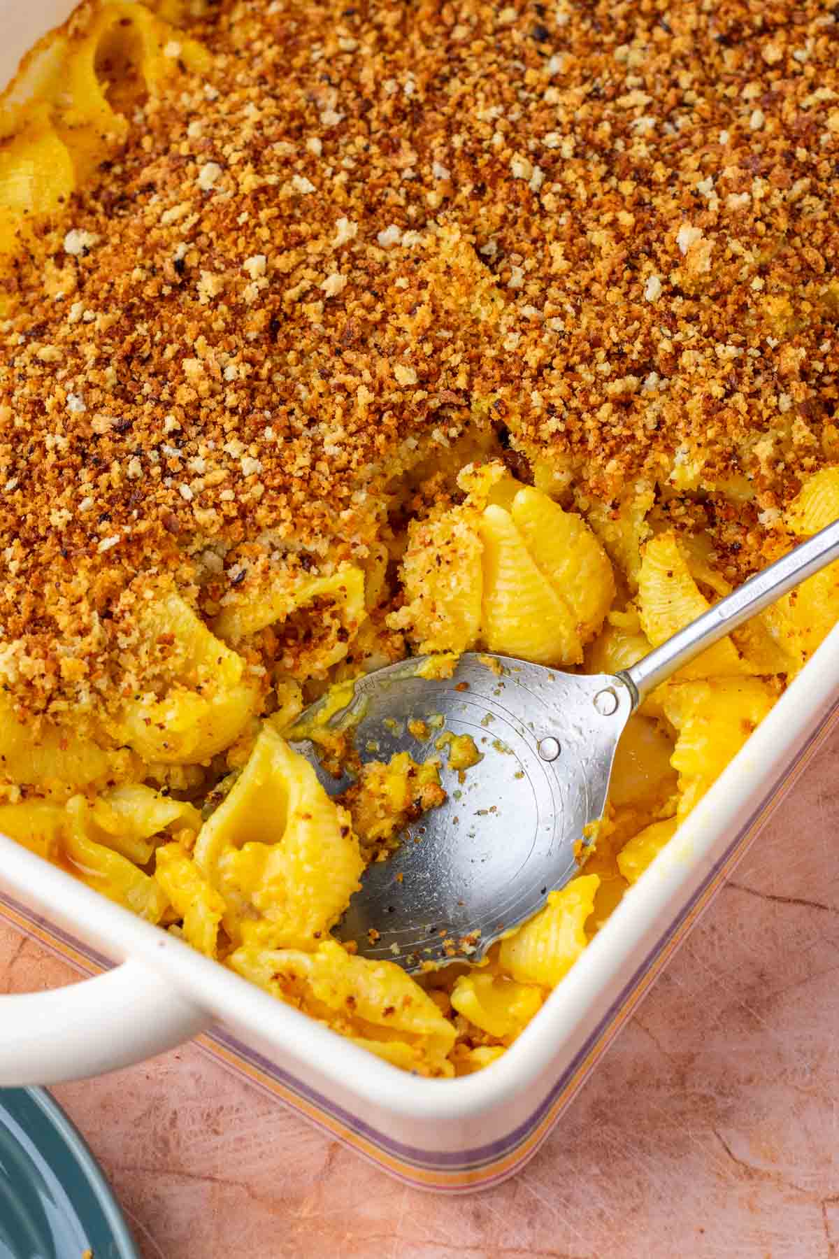 Large spoon in a baking dish of baked sourdough mac and cheese with sourdough breadcrumbs.