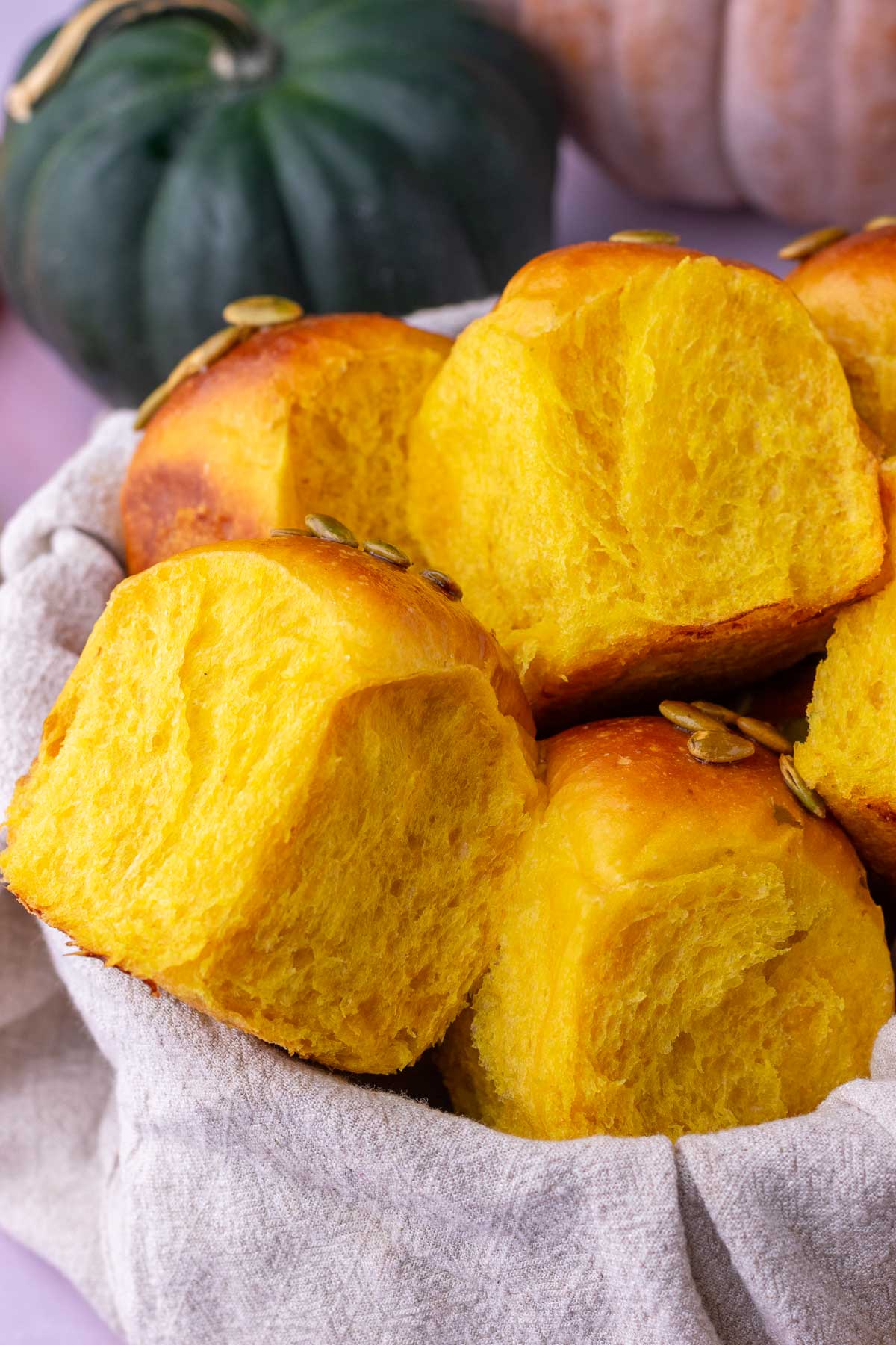 A basket of sourdough pumpkin dinner rolls with pumpkins in the background.