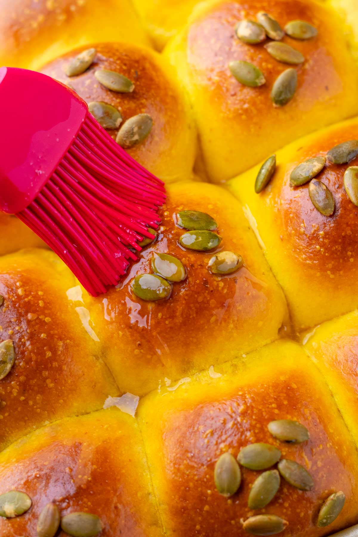 Brushing sourdough pumpkin dinner rolls with honey butter on top.