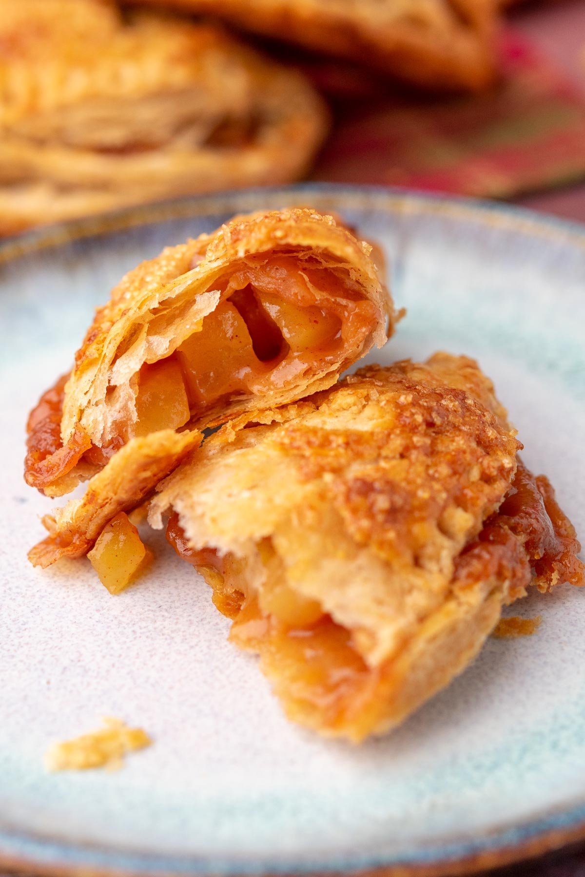 Up close image of a sourdough apple hand pie torn in half on a plate with visible apple filling and flaky crust.