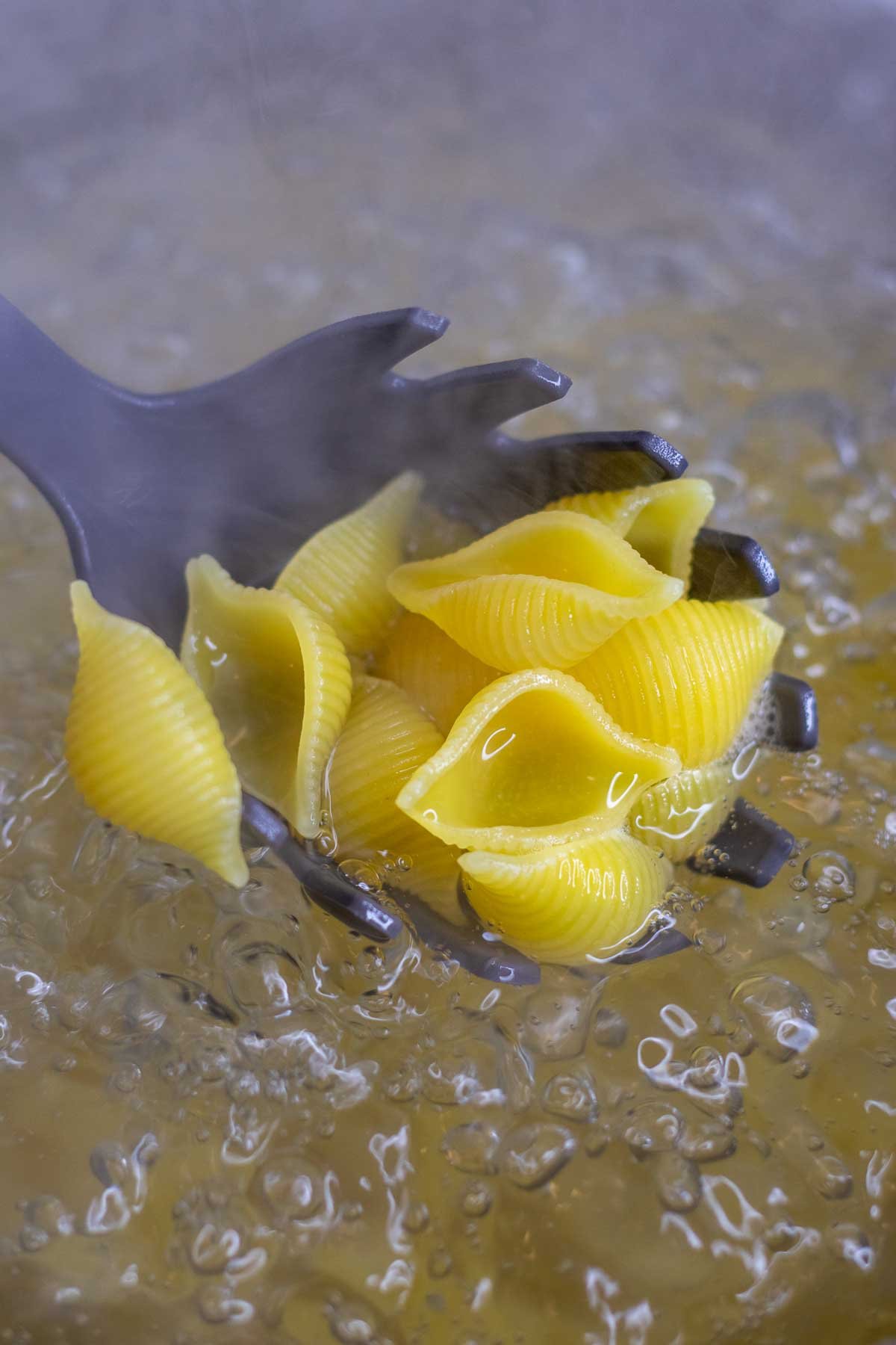 Cooked pasta shells in boiling water with a pasta scoop.