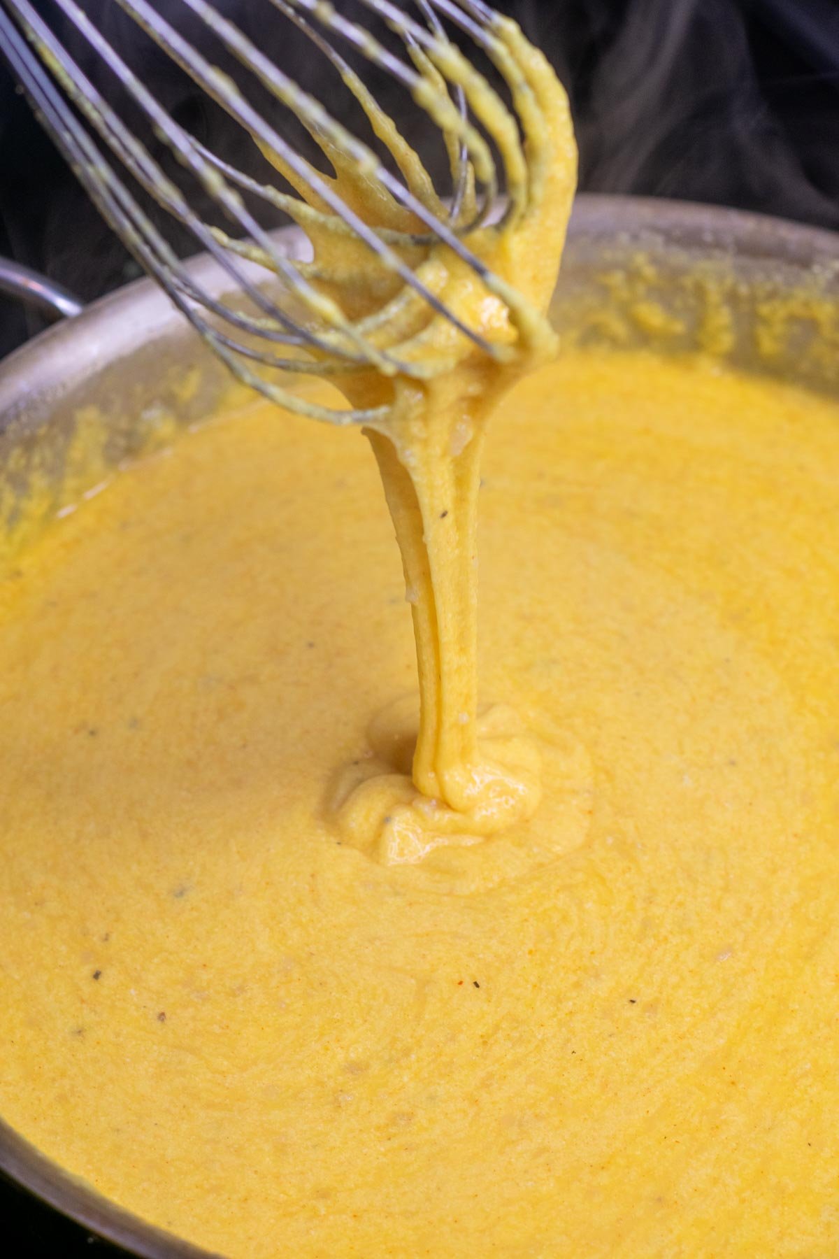 Melted cheese for sourdough mac and cheese in a pot with a whisk showing the cheese pull.