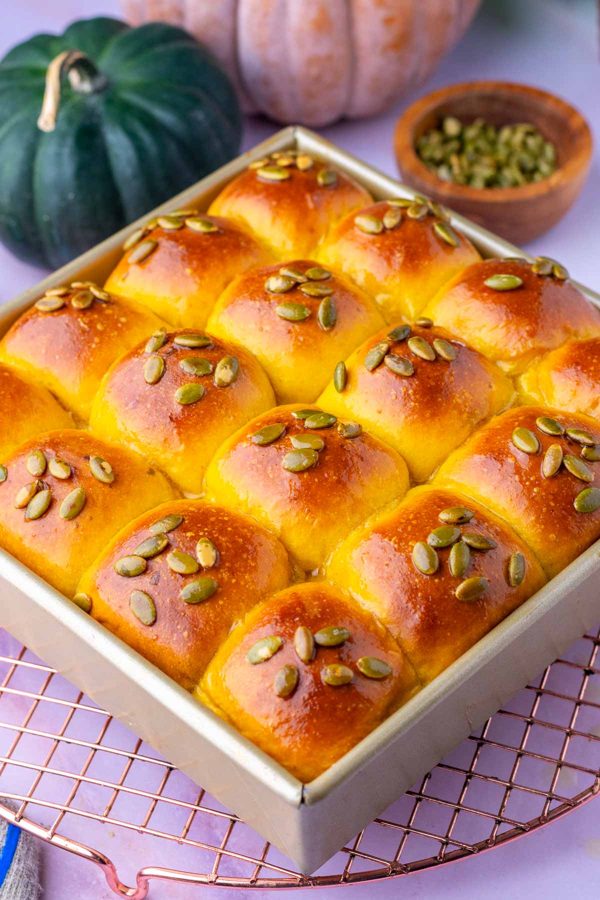 Pan of sourdough pumpkin dinner rolls with pumpkin seeds and pumpkins surrounding it.