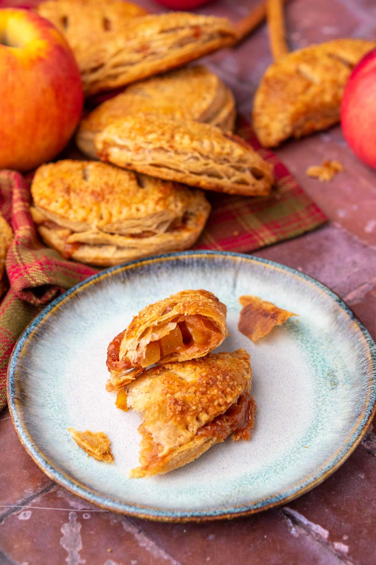 Sourdough apple hand pie torn in half on a plate with more hand pies and apples in the background.