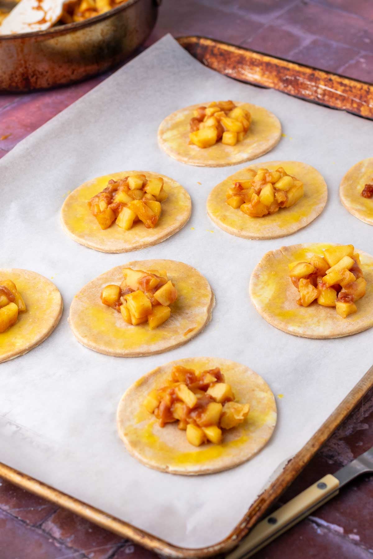 Filling sourdough apple hand pie rounds with apple filling on a sheet pan.