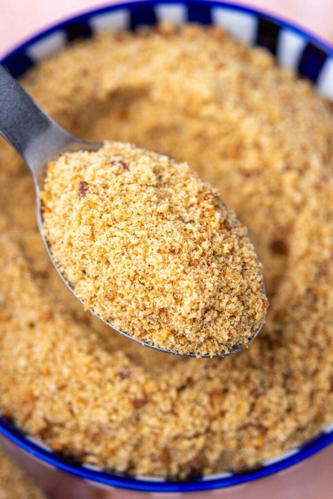 Spoon of homemade sourdough breadcrumbs over a bowl of breadcrumbs.