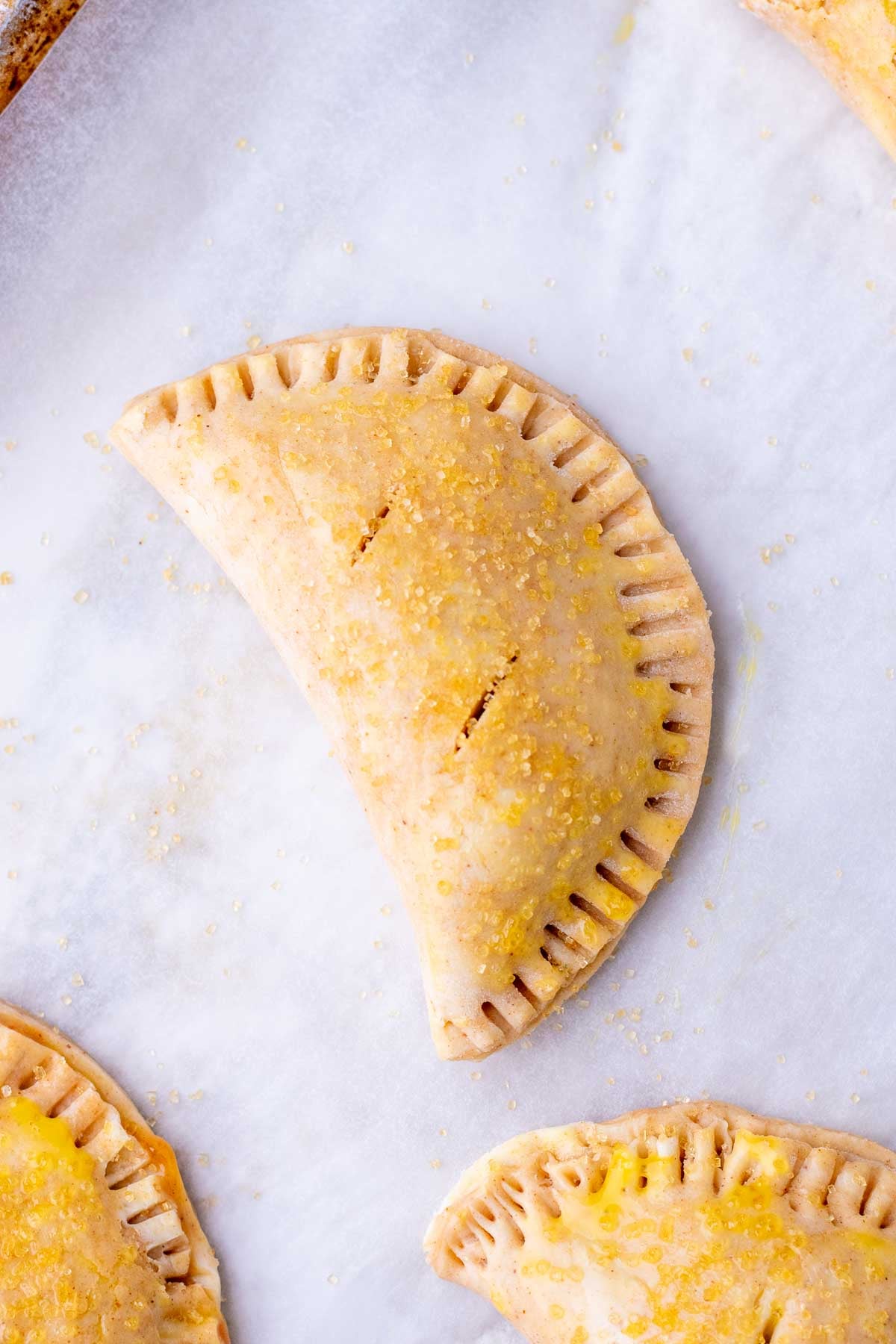 Unbaked sourdough apple hand pie with egg wash and raw sugar topping on a sheet pan.