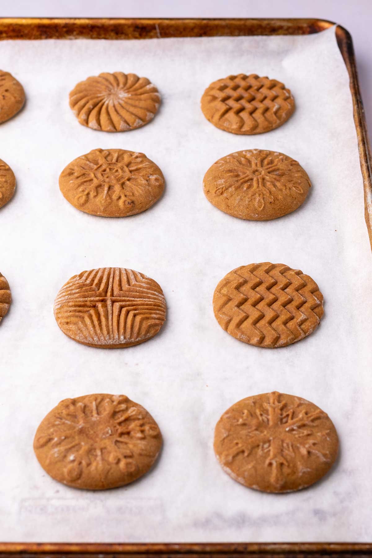 Baked sourdough gingerbread cookies with snowflake and geometric patterns on a baking sheet before glaze.