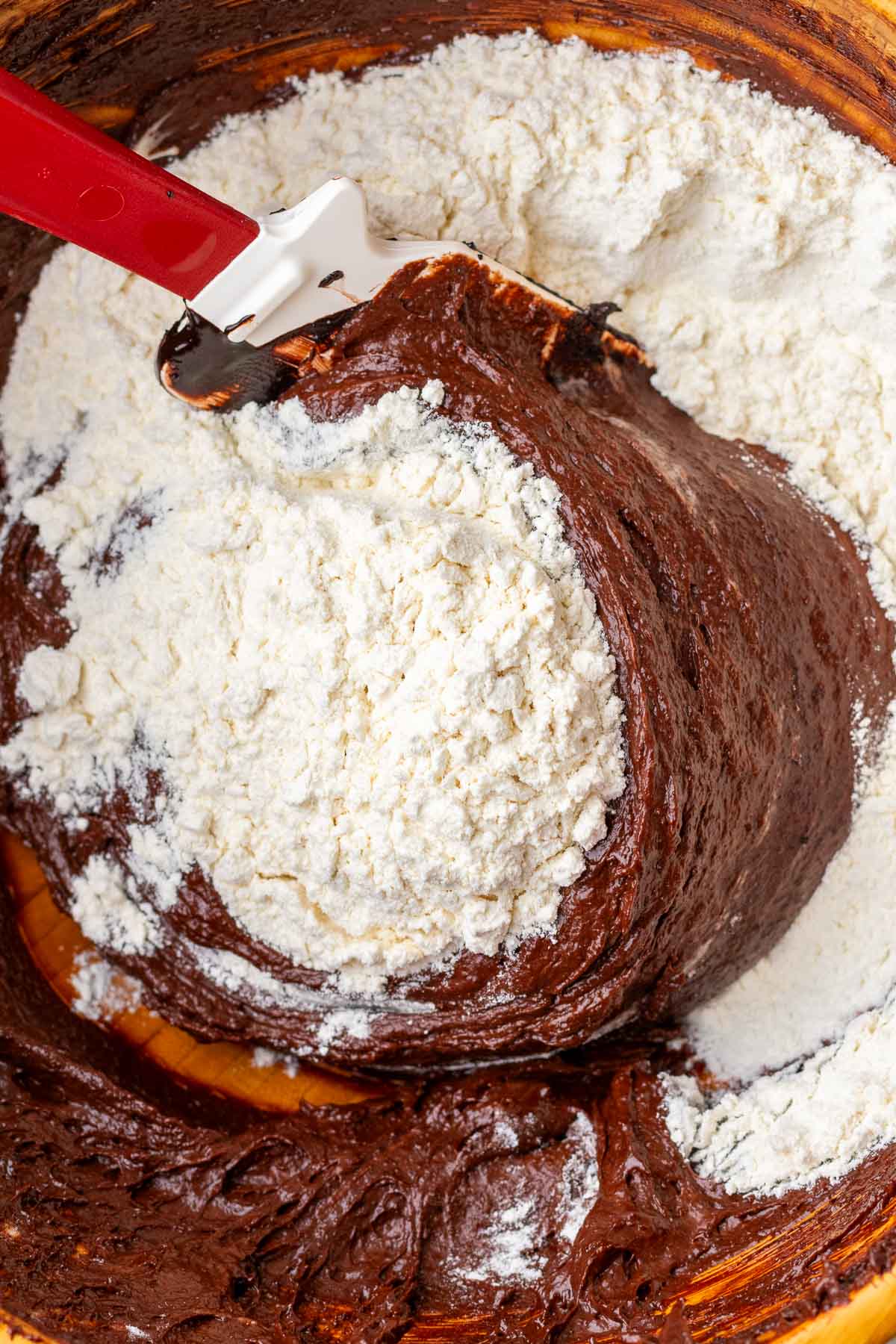 Folding dry ingredients into sourdough chocolate crinkle cookie dough in a large bowl with a spatula.