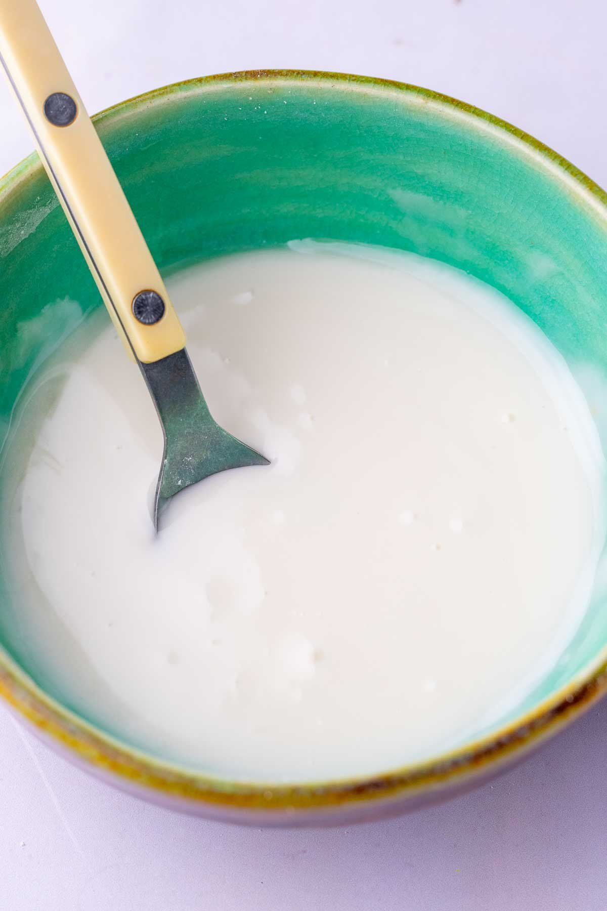 Glaze for soft glazed sourdough gingerbread cookies in a bowl with a spoon.