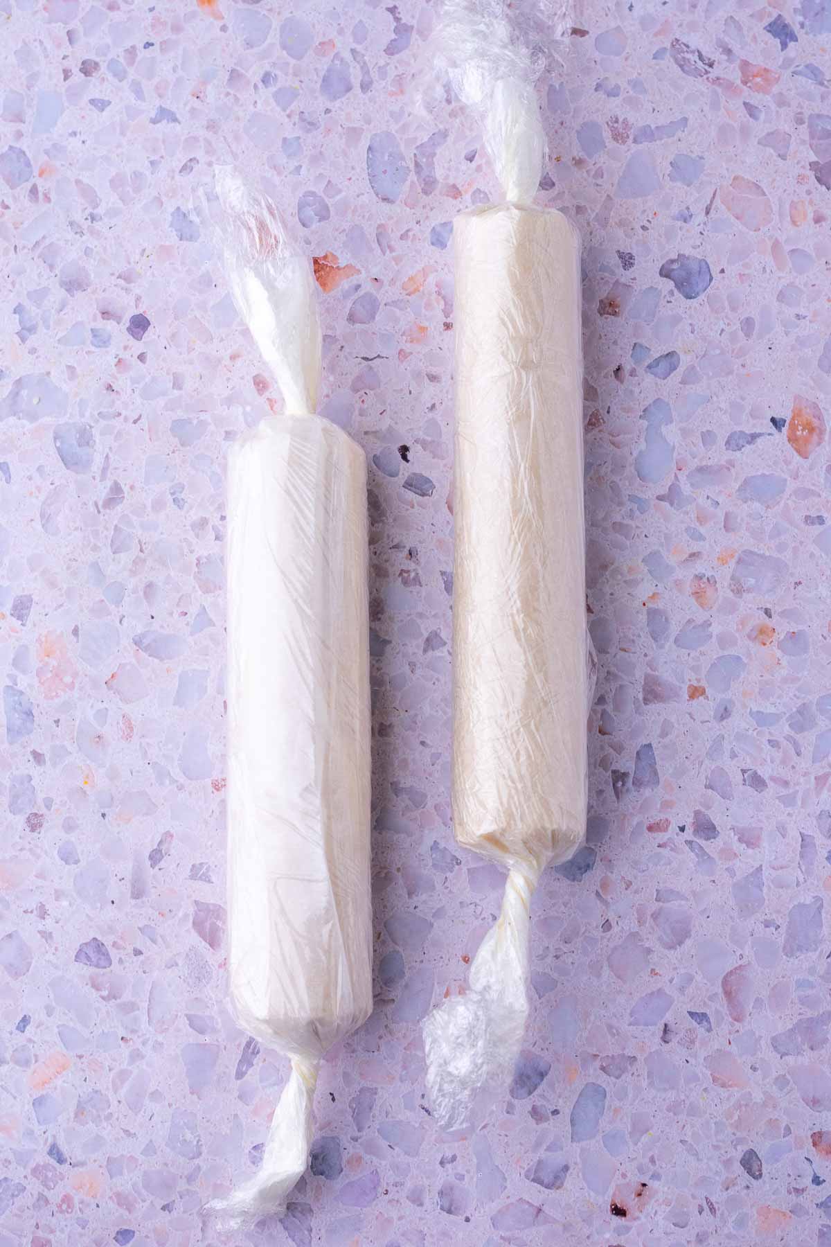 Two logs of sourdough shortbread cookies wrapped in parchment paper and plastic wrap.