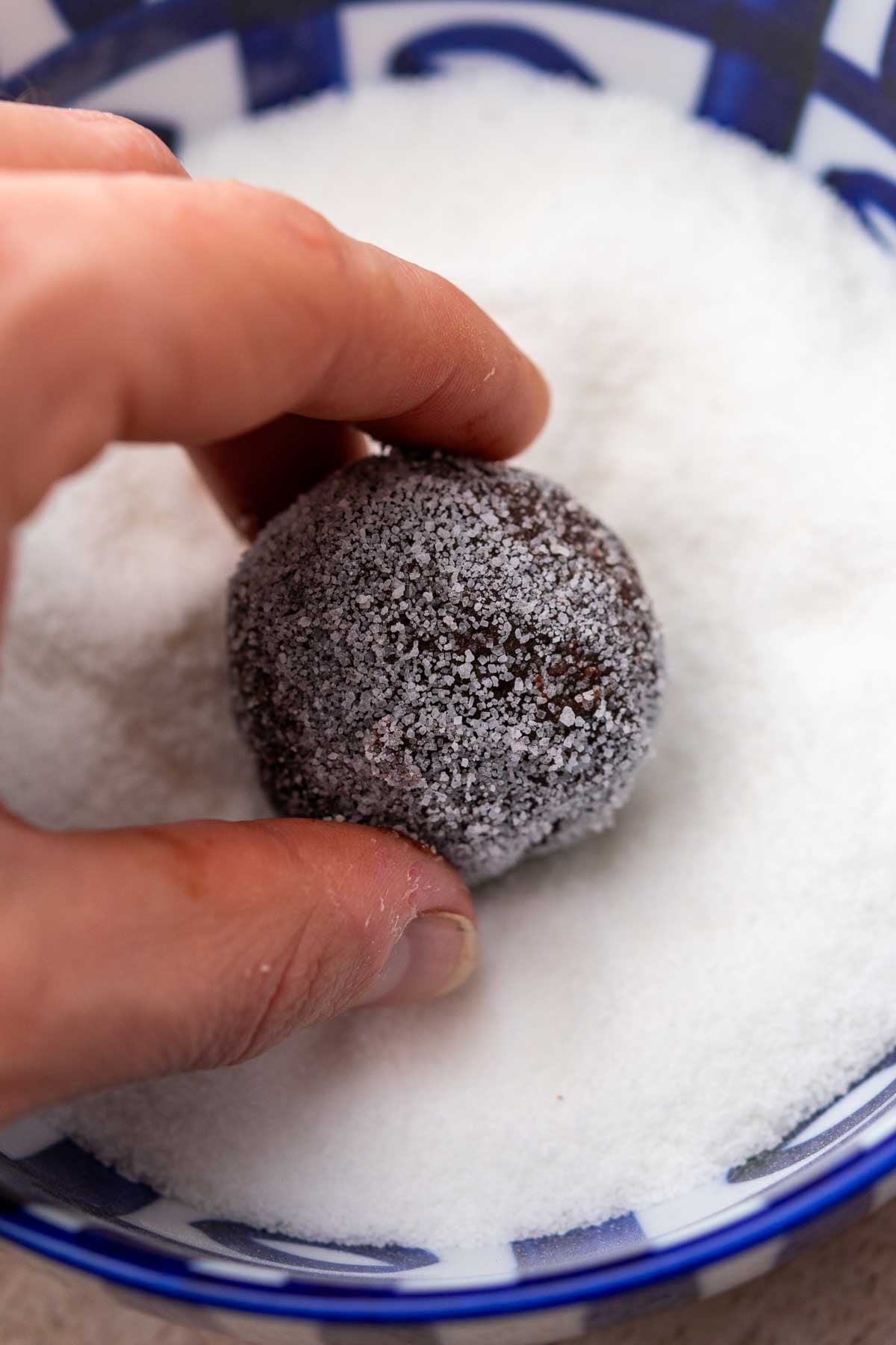 Hand rolling a sourdough chocolate crinkle cookie in a bowl of granulated sugar.