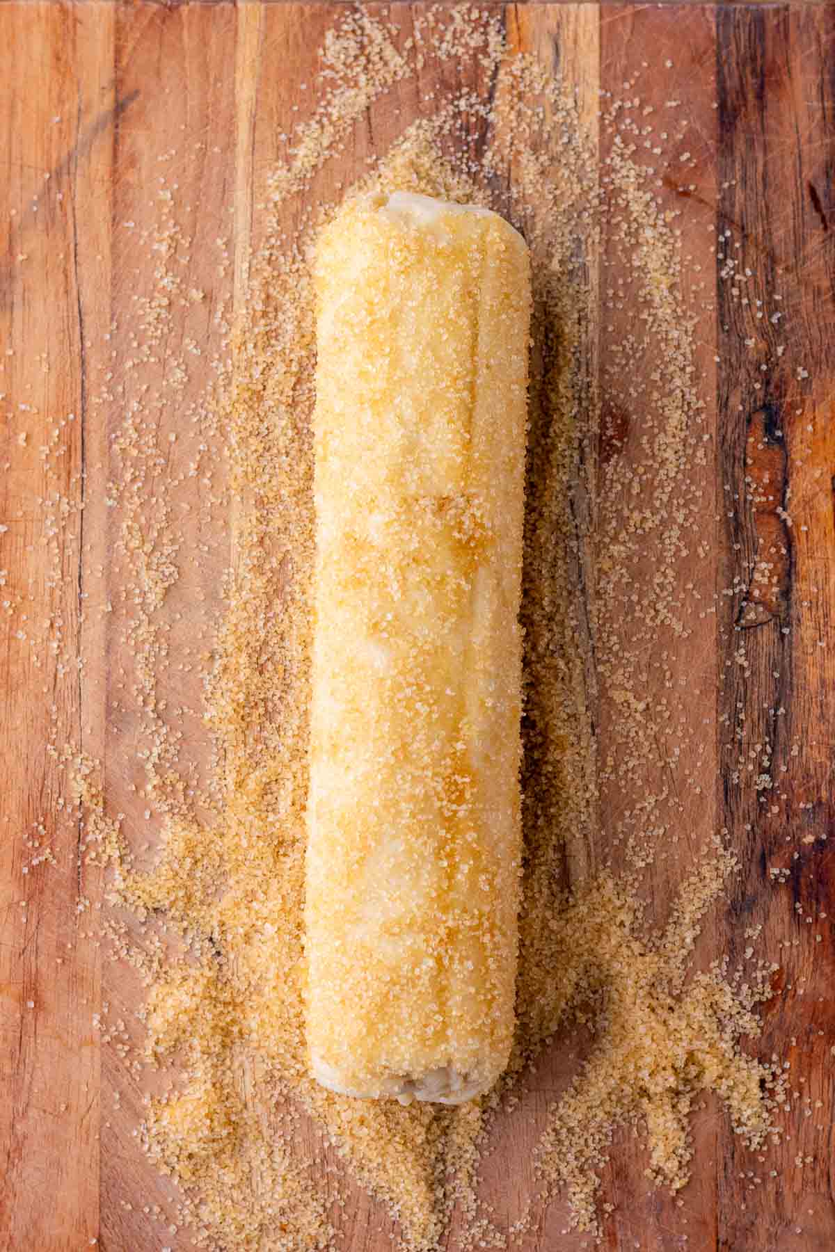 Log of sourdough shortbread cookies on a wooden cutting board with raw sugar.