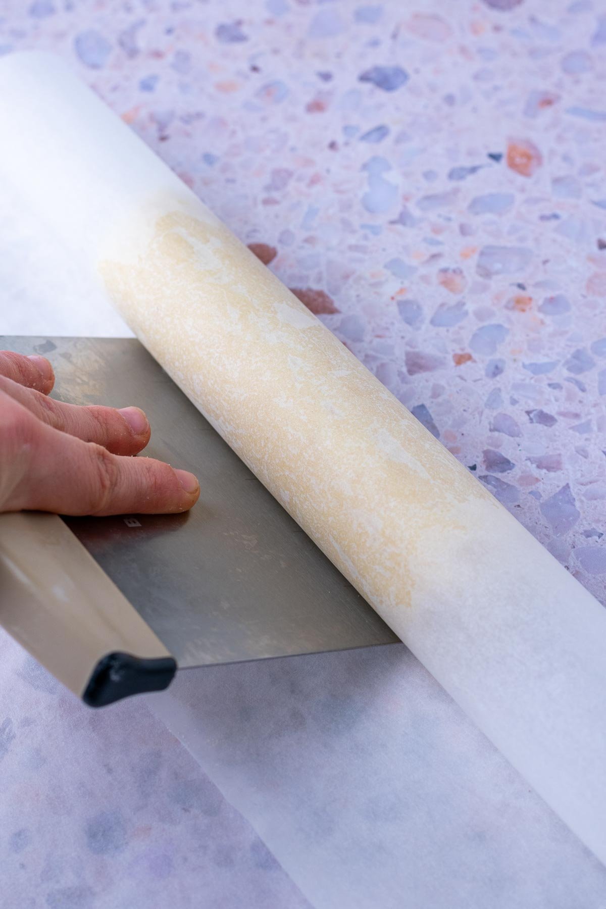 Rolling sourdough shortbread cookies into a log of parchment paper with a bench scraper.