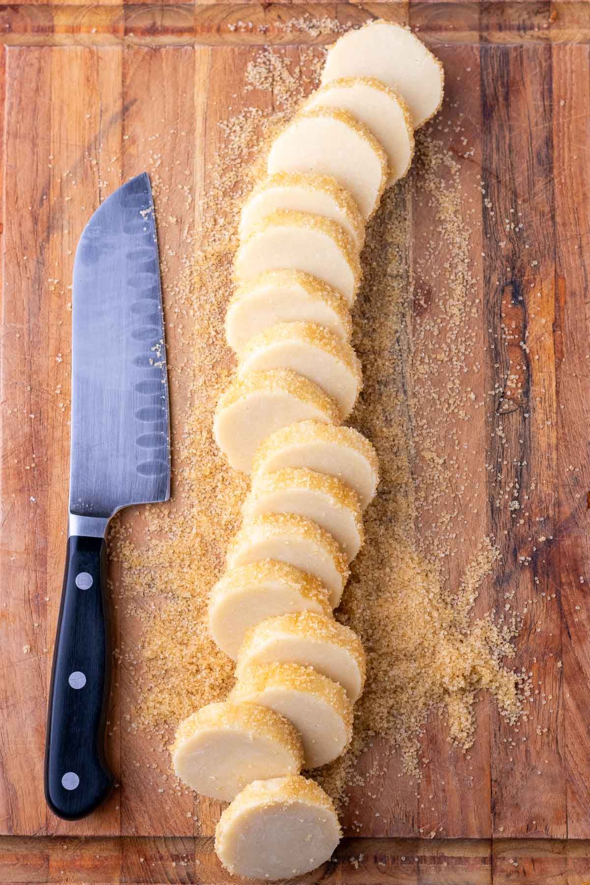 Sliced sourdough shortbread cookies on a wooden cutting board with a knife.