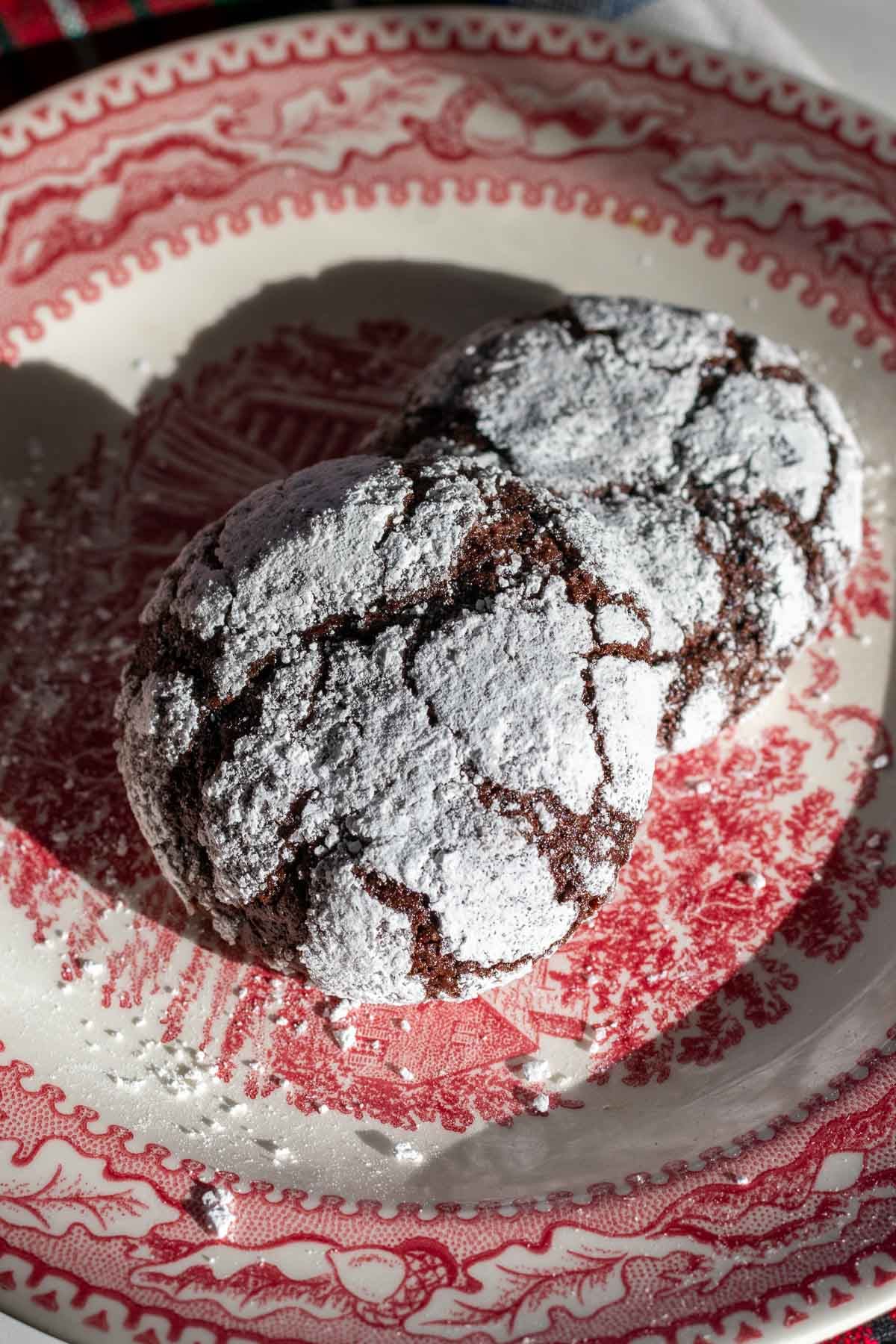 Two sourdough chocolate crinkle cookies on a red and white plate.