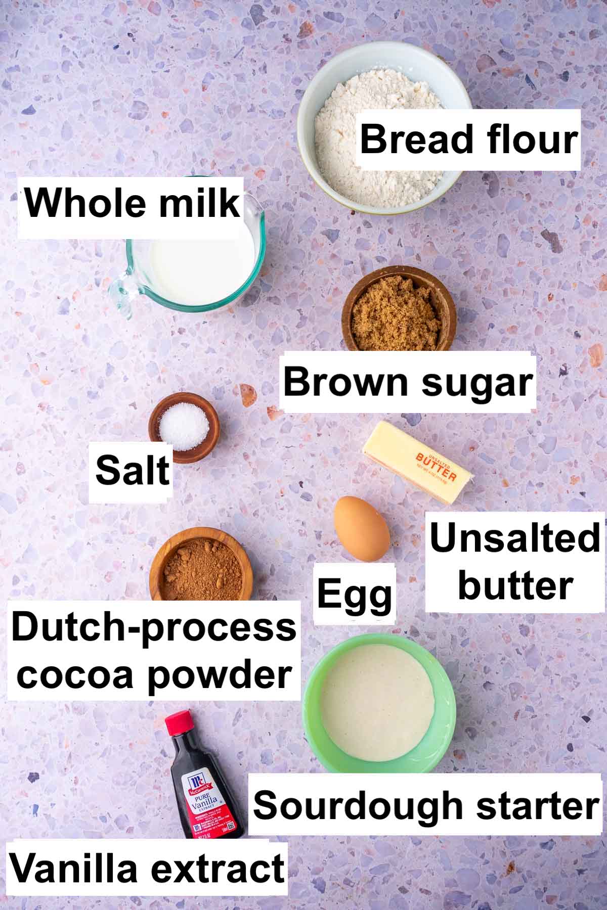 Labeled bowls of ingredients needed for sourdough chocolate brioche including bread flour, whole milk, brown sugar, salt, egg, unsalted butter, dutch-process cocoa powder, sourdough starter, and vanilla extract.