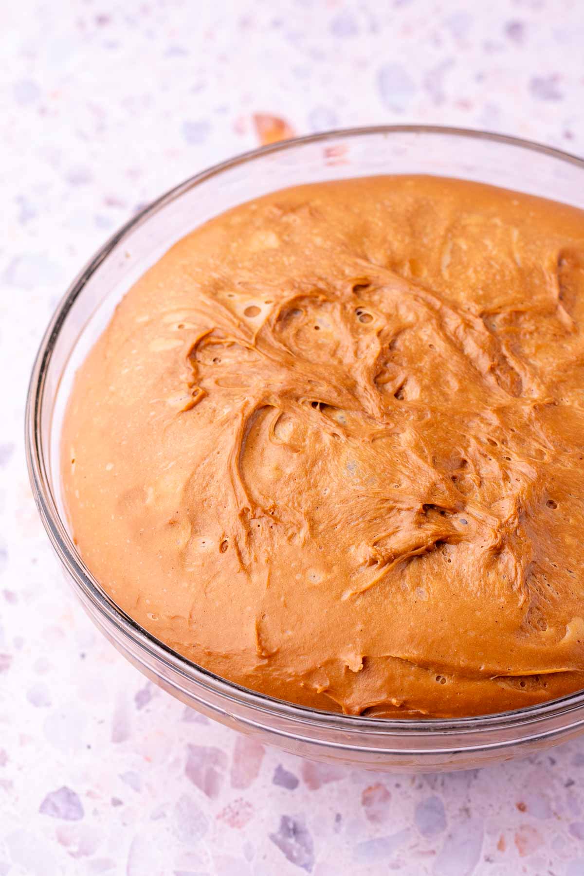 Sourdough chocolate brioche dough in a glass mixing bowl at the end of bulk fermentation.