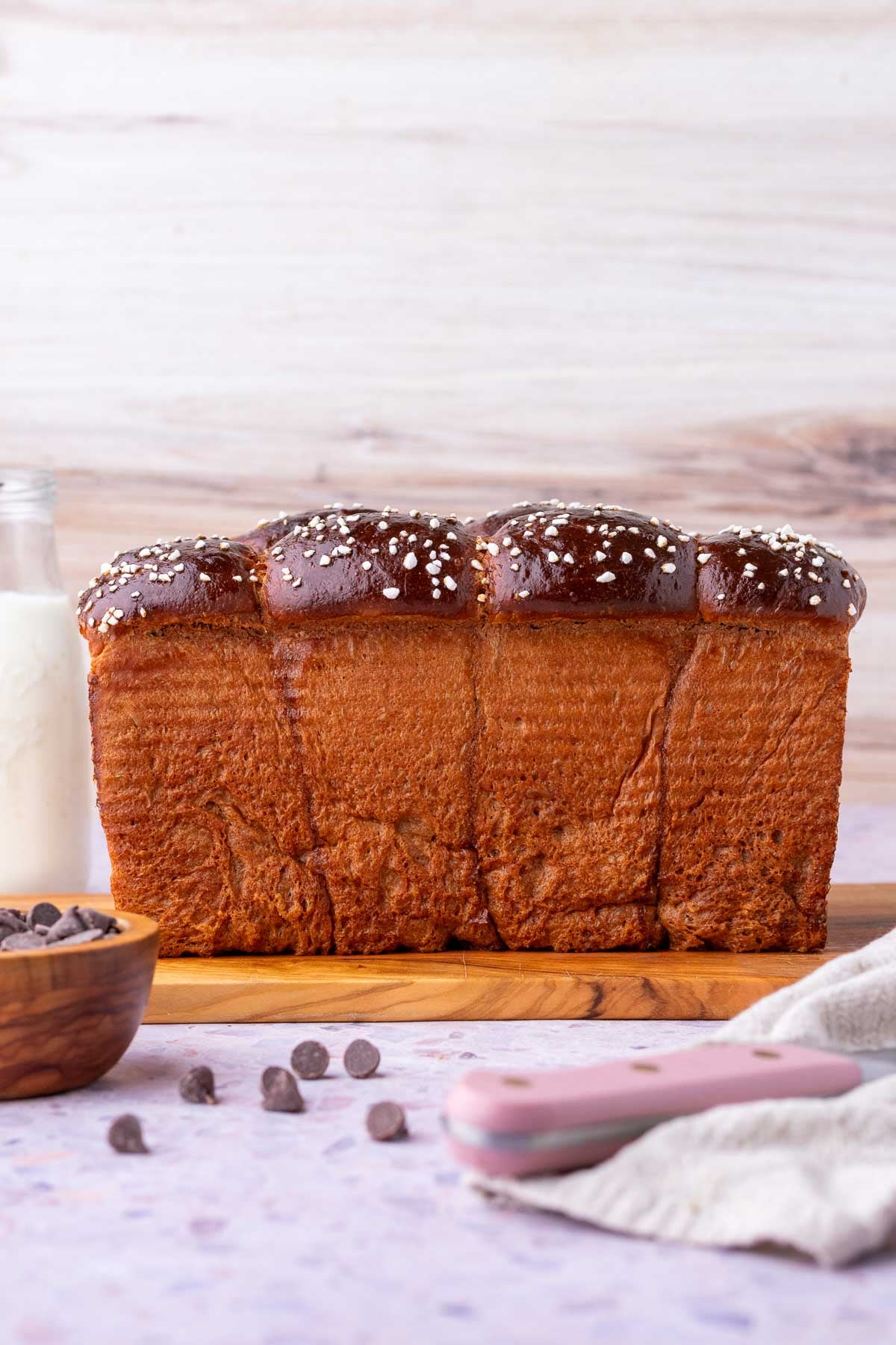 Side profile of sourdough chocolate brioche bread on a cutting board with chocolate chips and a bread knife.