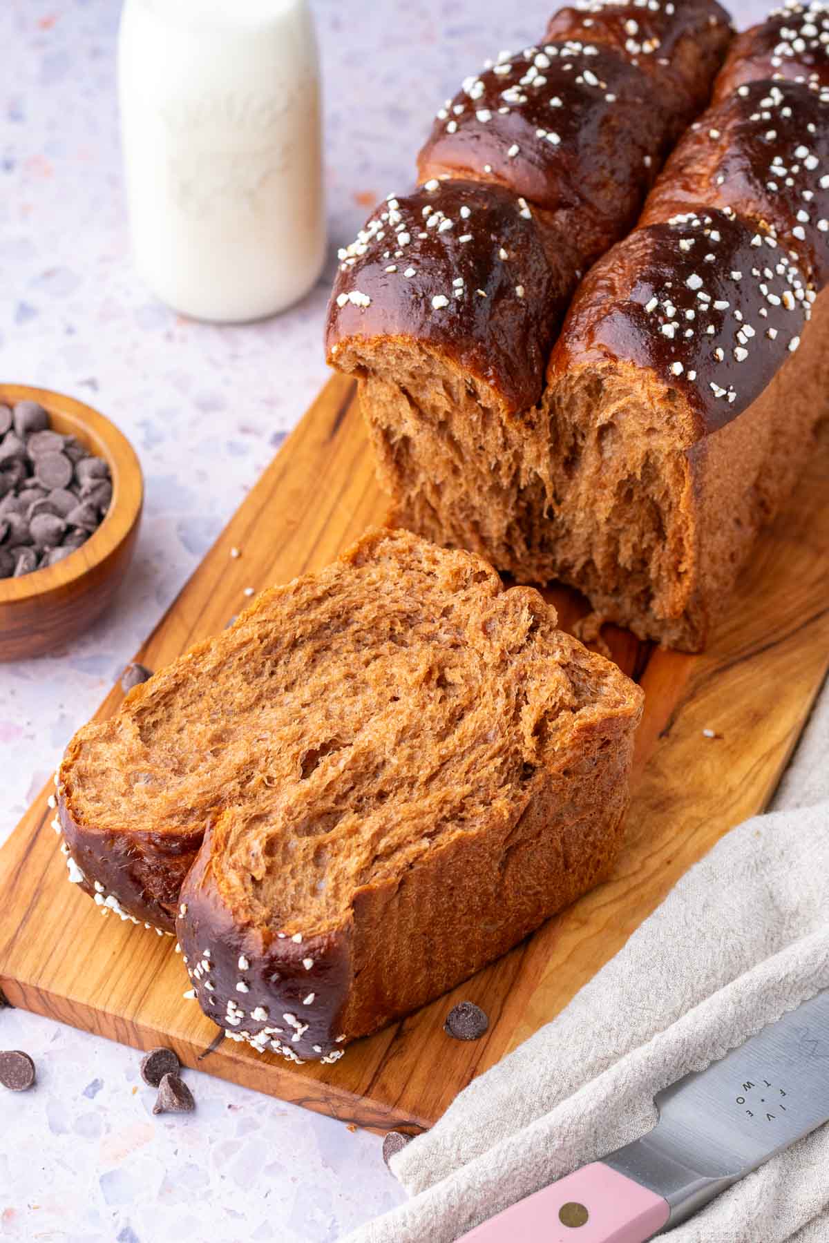 Sliced sourdough chocolate brioche bread on a cutting board with chocolate chips and a glass of milk in the background.