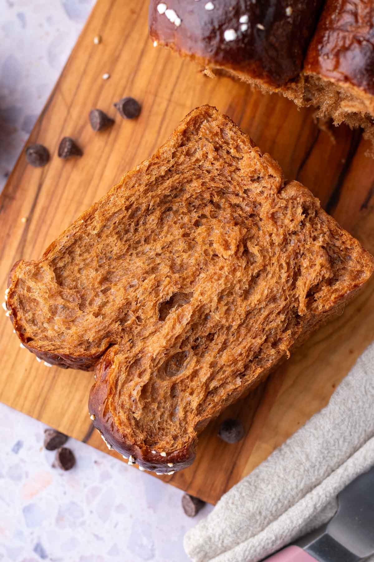 Slice of sourdough chocolate brioche on a cutting board surrounded by chocolate chips.