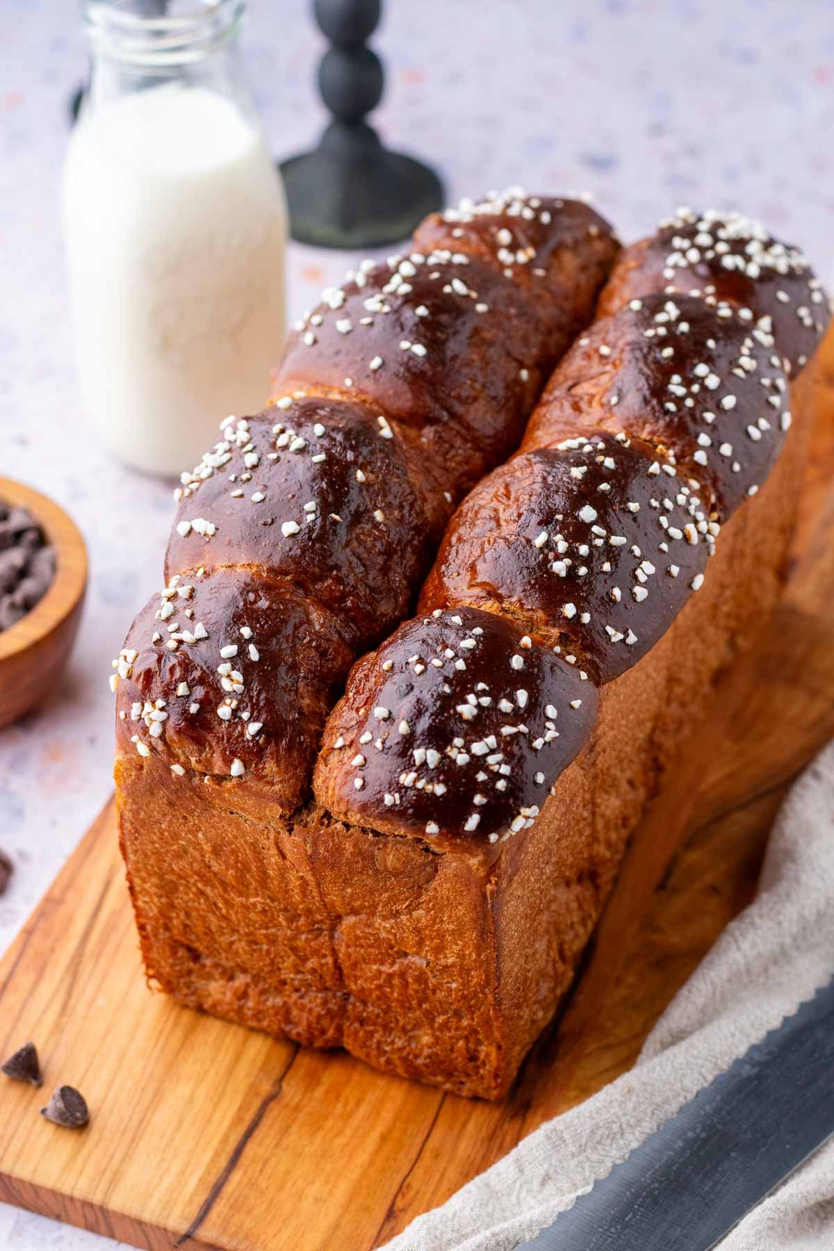 Baked sourdough chocolate brioche bread on a cutting board with a glass of milk in the background.