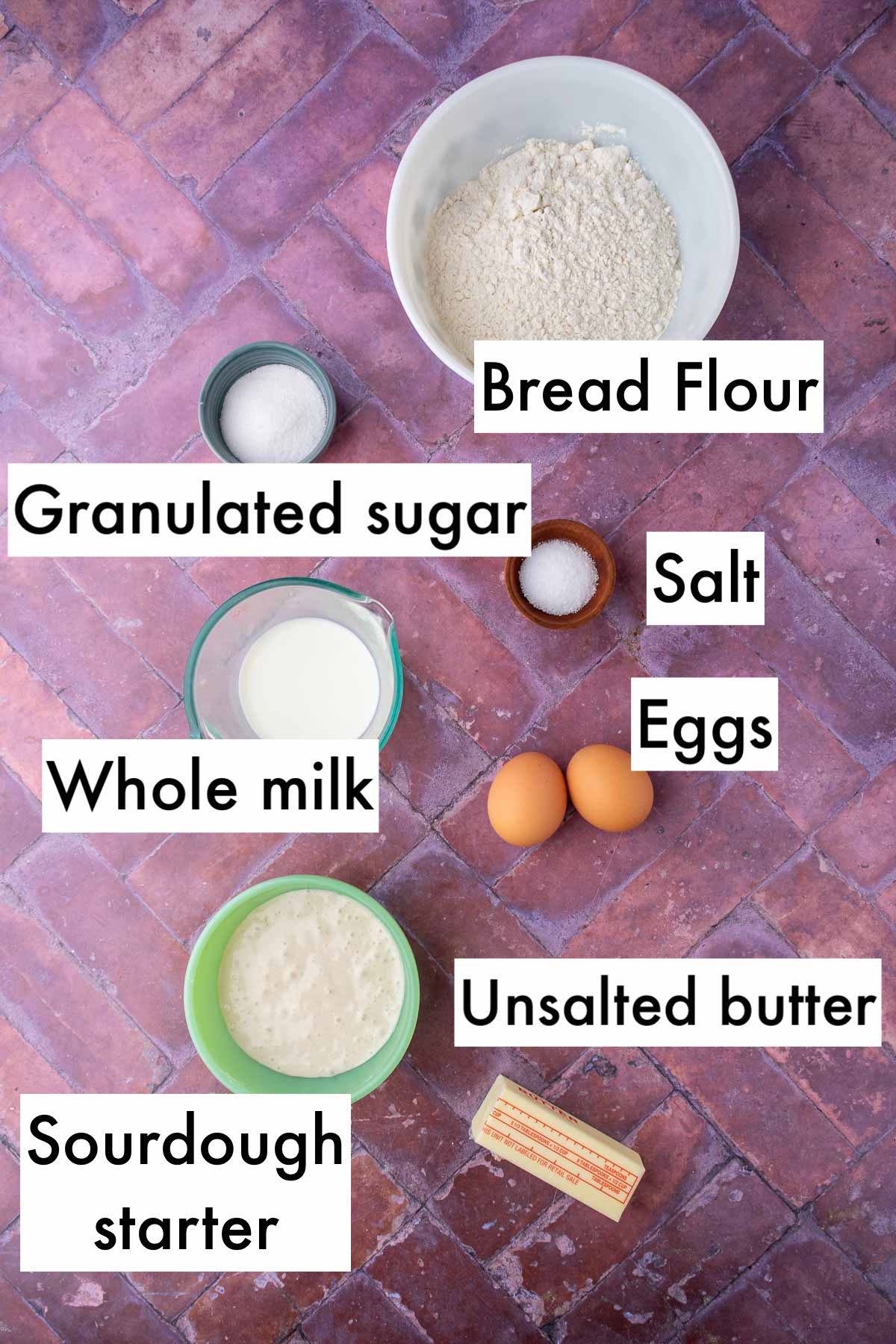 Labeled bowls of ingredients needed for cloverleaf sourdough dinner rolls including bread flour, sugar, salt, eggs, milk, sourdough starter, and butter.