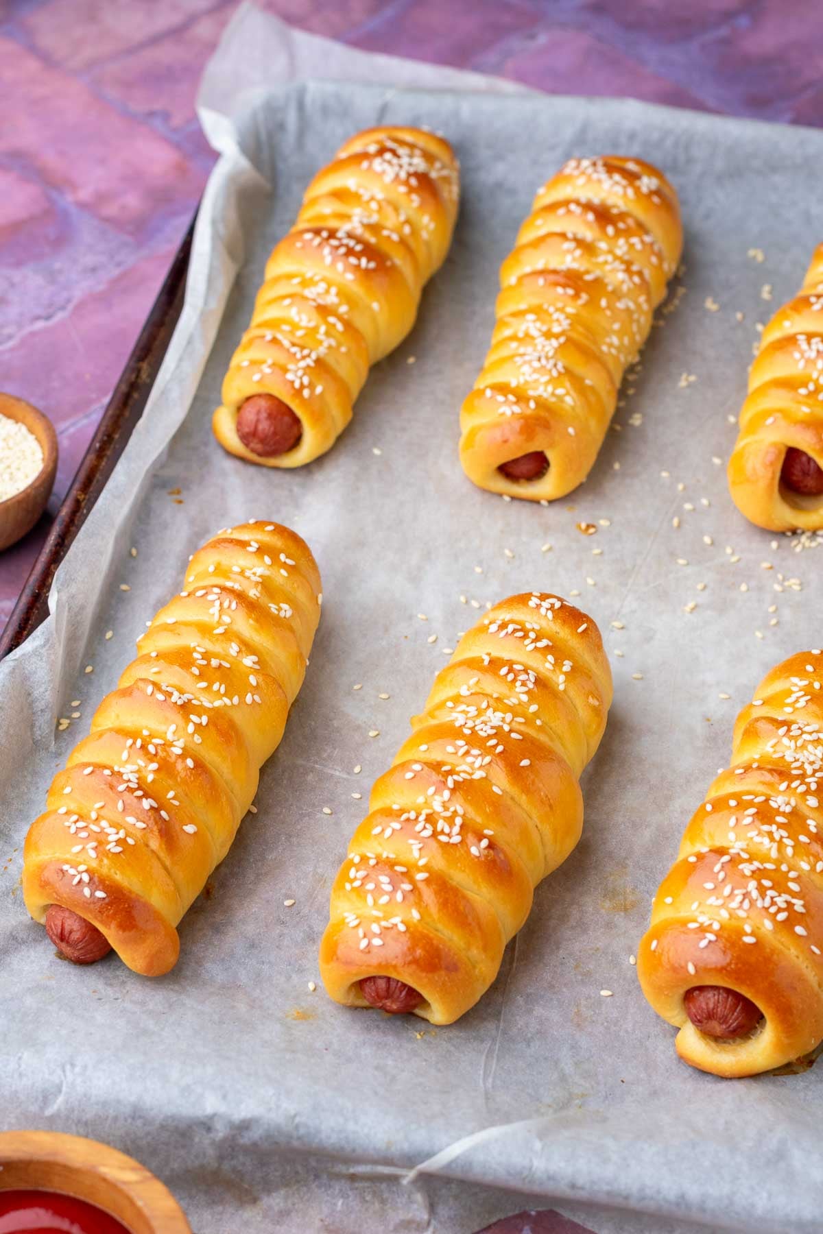 Baked sourdough pigs in a blanket on a sheet pan with parchment paper.