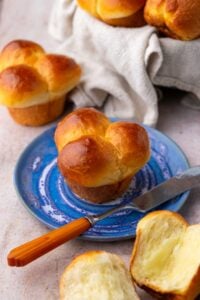 Cloverleaf sourdough dinner roll on a blue plate with a butter knife surrounded by more dinner rolls.