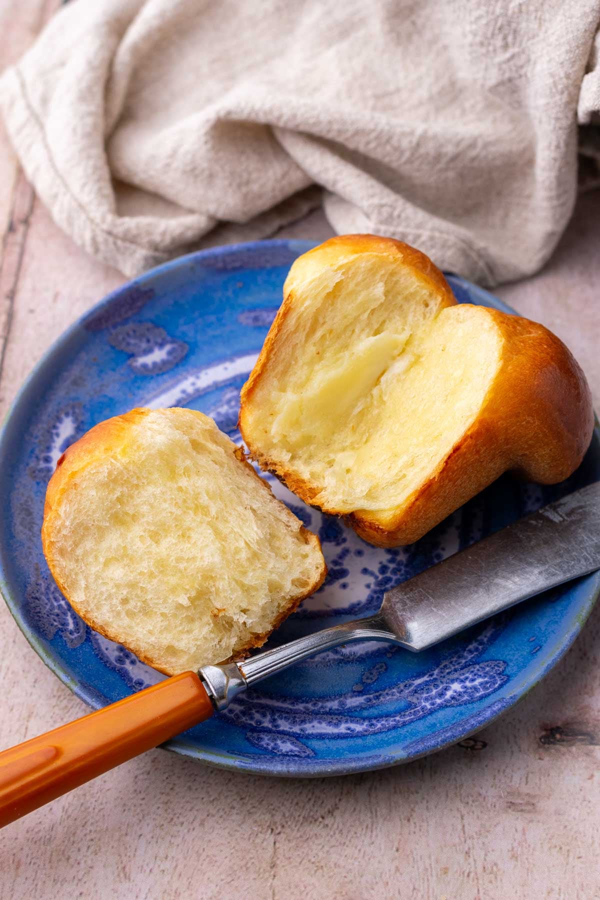 Cloverleaf sourdough dinner roll opened on a plate with butter and a butter knife.
