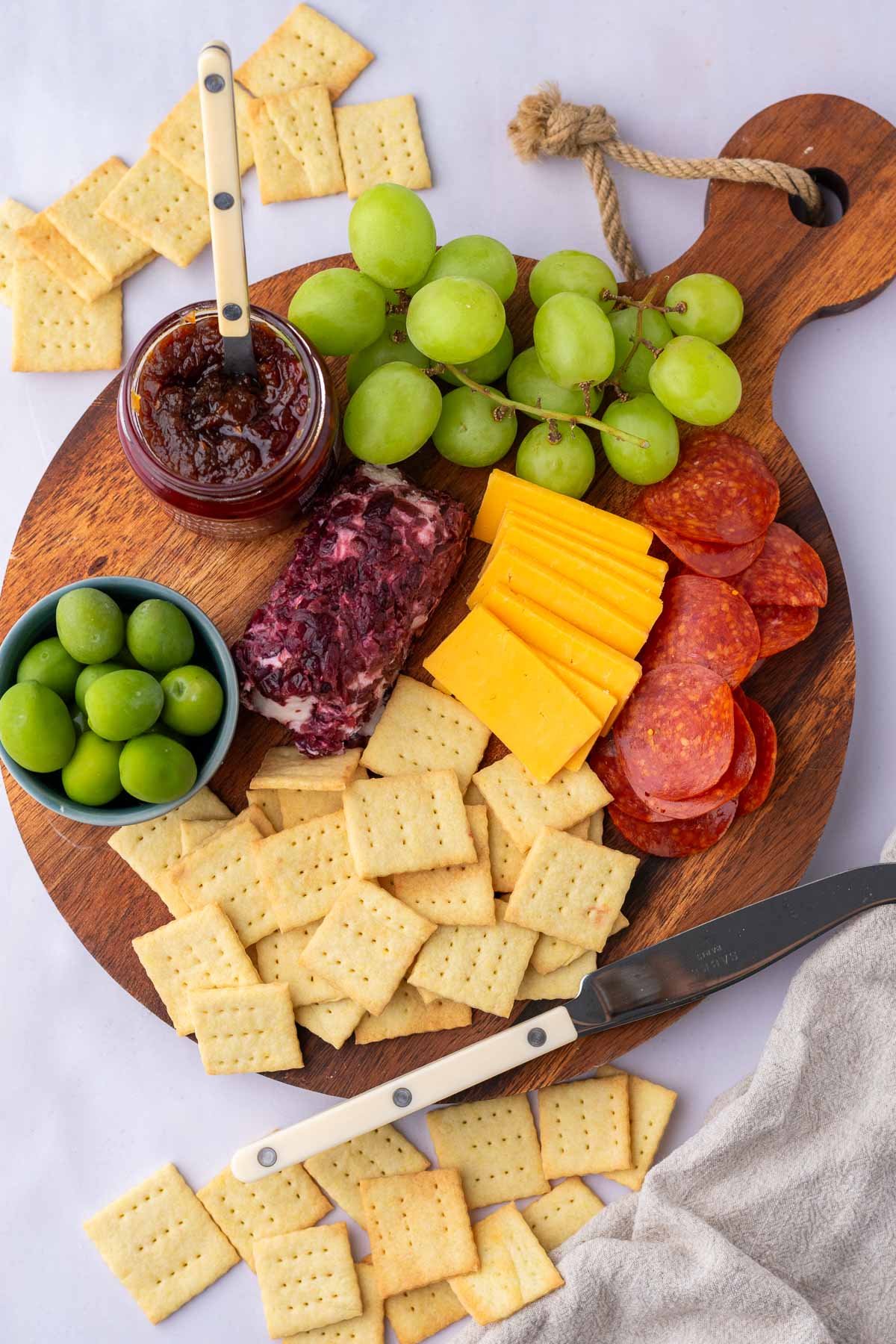 Overhead of Sourdough Butter Crackers on a cheese plate with grapes, olives, jam, cheeses, and pepperoni.