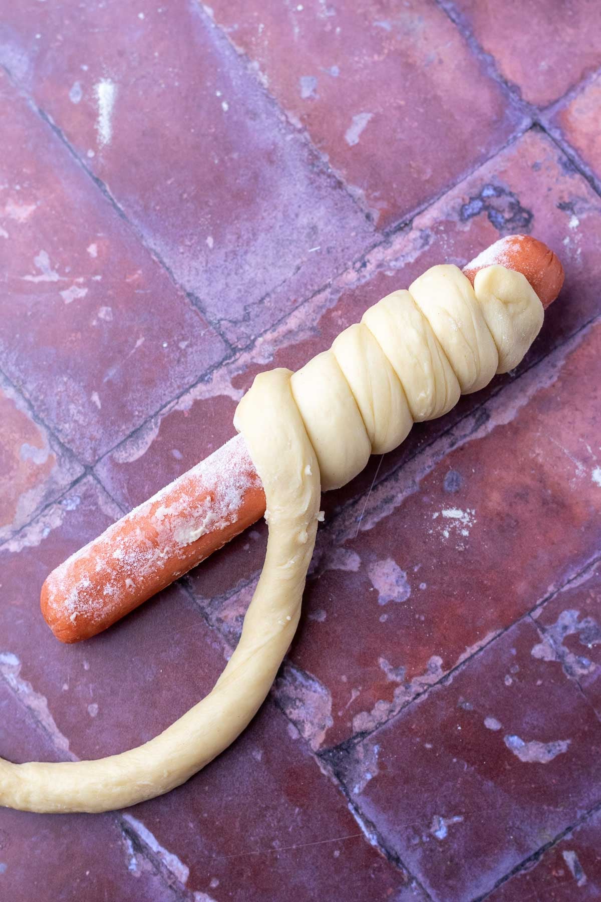 Wrapping sourdough brioche dough around a hot dog for shaping sourdough pigs in a blanket.