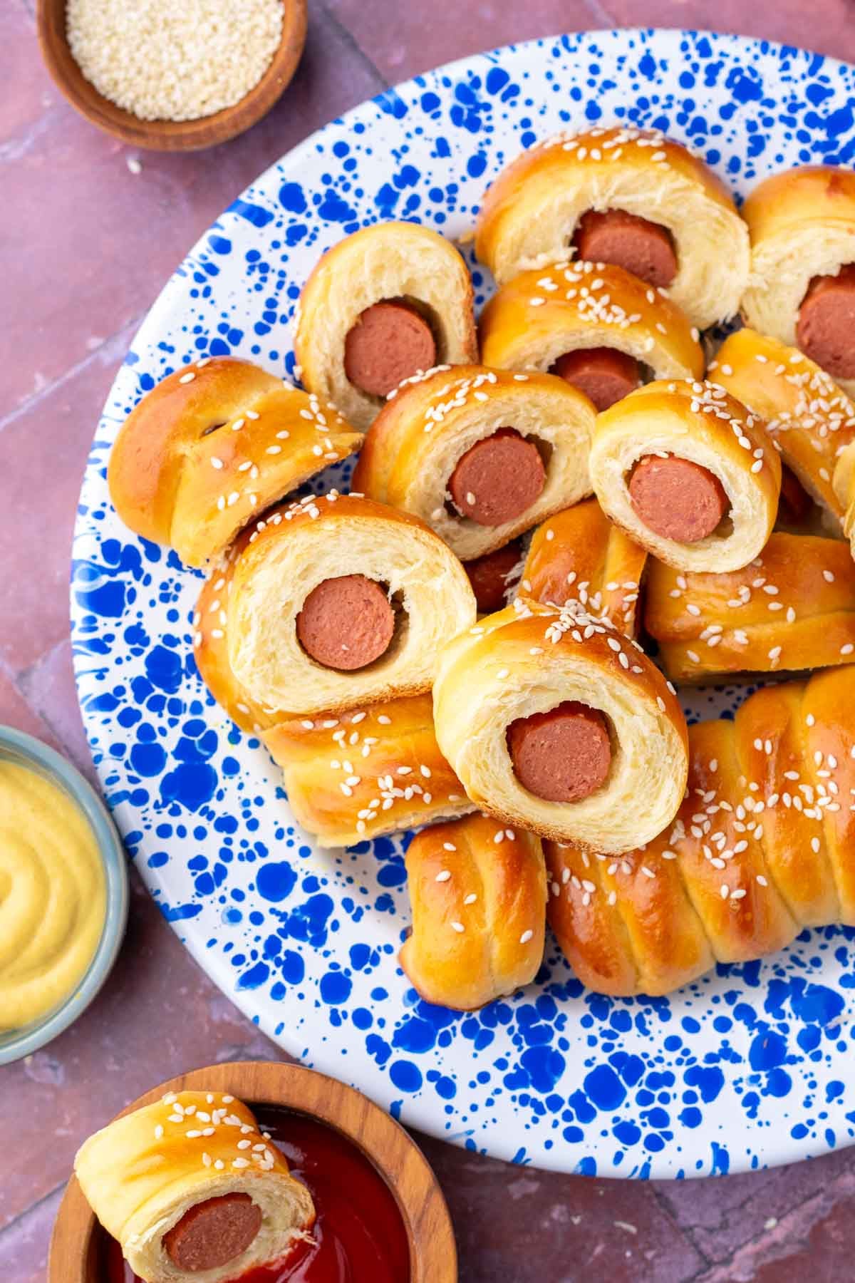 Blue and white enamel plate of sourdough pigs in a blanket surrounded by bowls of condiments.