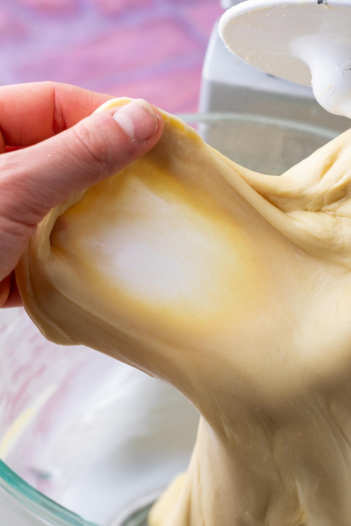 Hand pulling sourdough brioche dough for windowpane test in a stand mixer.