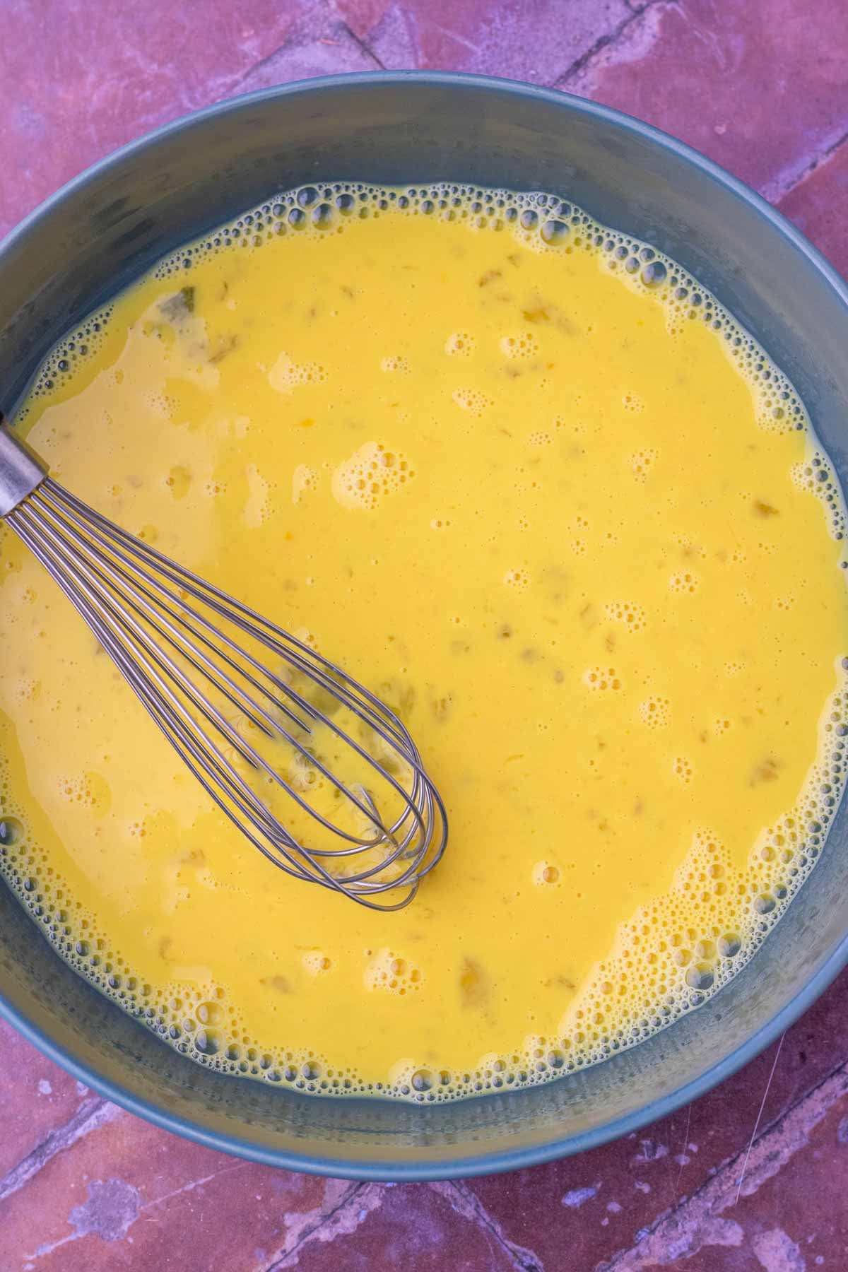 Whisked egg mixture for sourdough french toast sticks in a bowl with a whisk.
