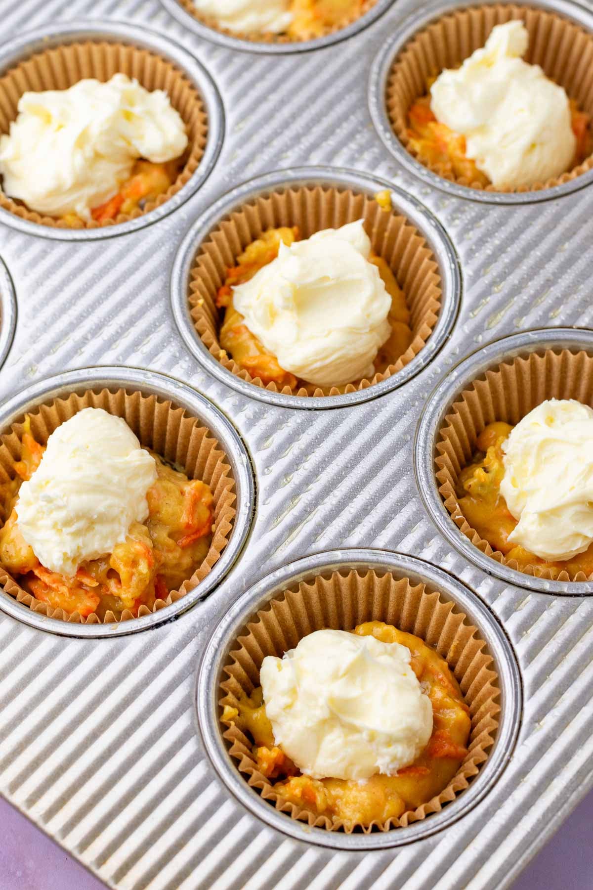 Filling sourdough carrot cake muffins in muffin pan with cream cheese.