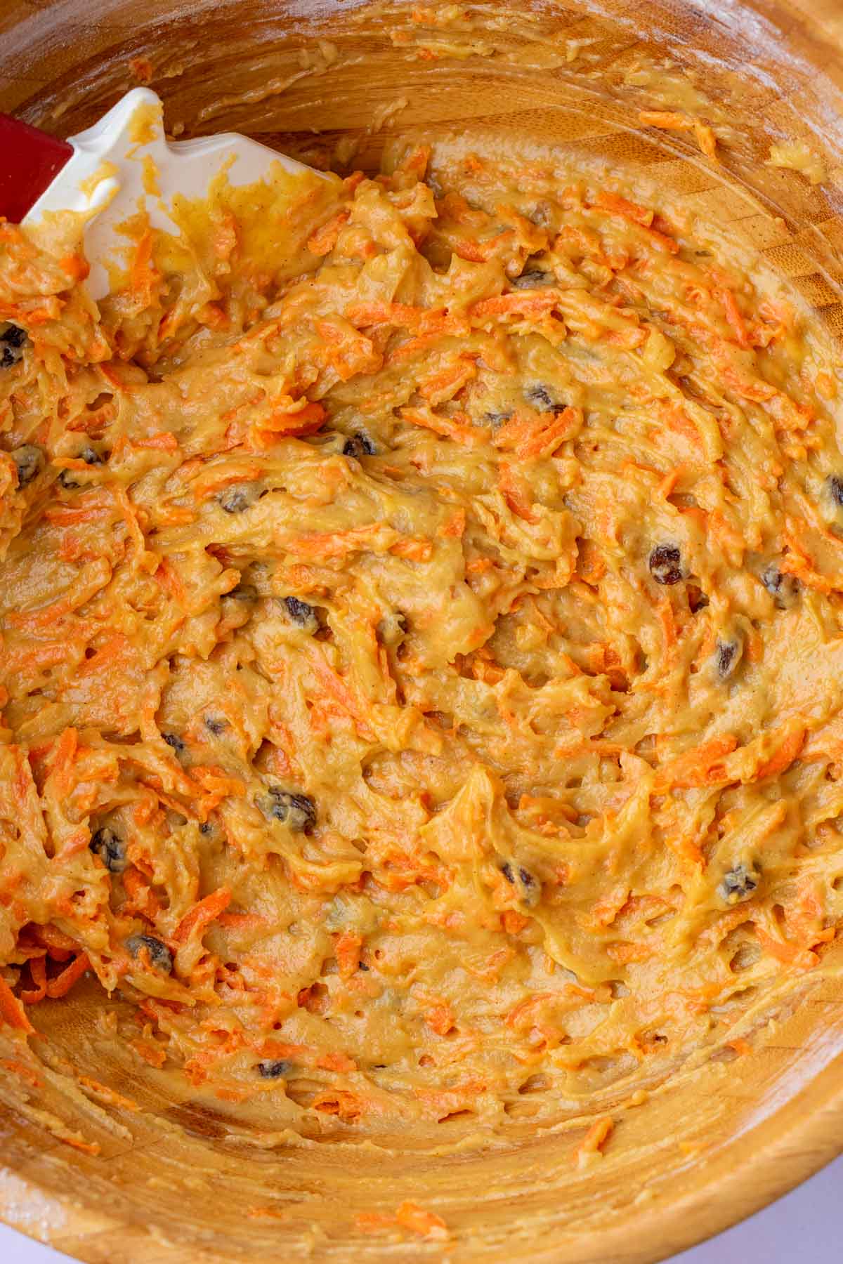Mixed sourdough carrot cake muffin batter in a bowl with a spatula.