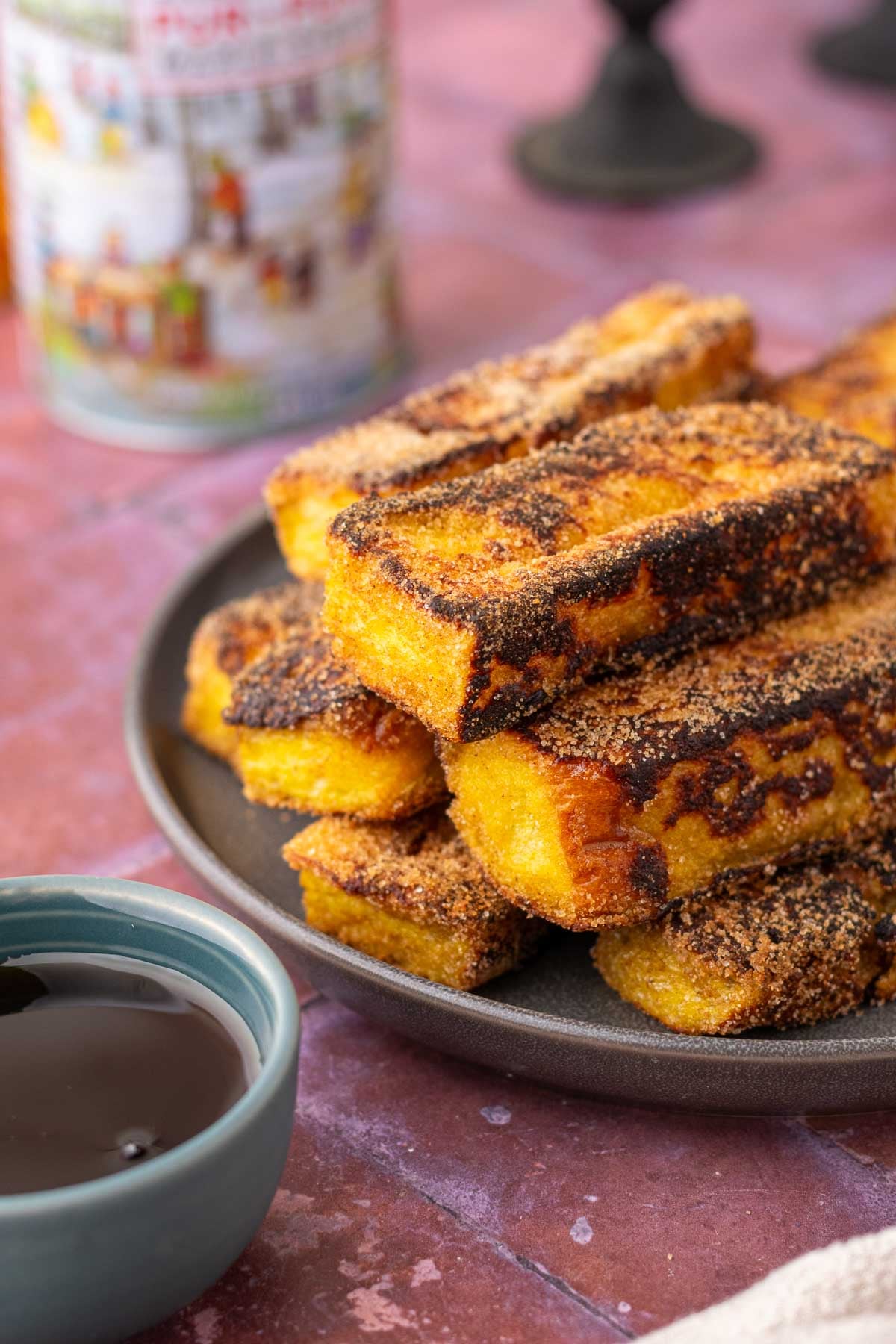 Stack of sourdough cinnamon french toast sticks on a plate with a small bowl of maple syrup.