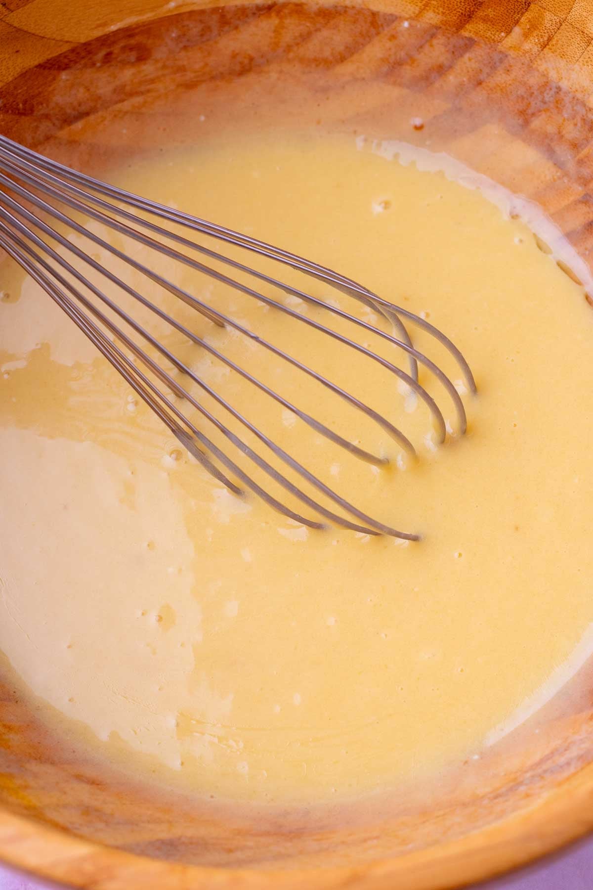 Whisk in a wooden bowl mixing wet ingredients for sourdough carrot cake muffins.