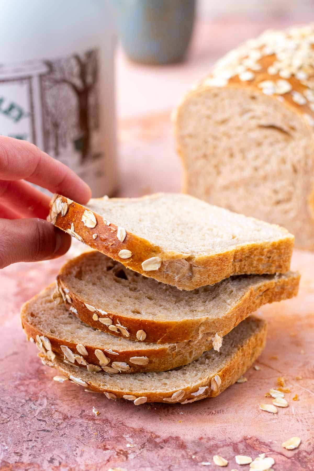 Hand picking up a slice of maple oat sourdough sandwich bread from a stack of slices.