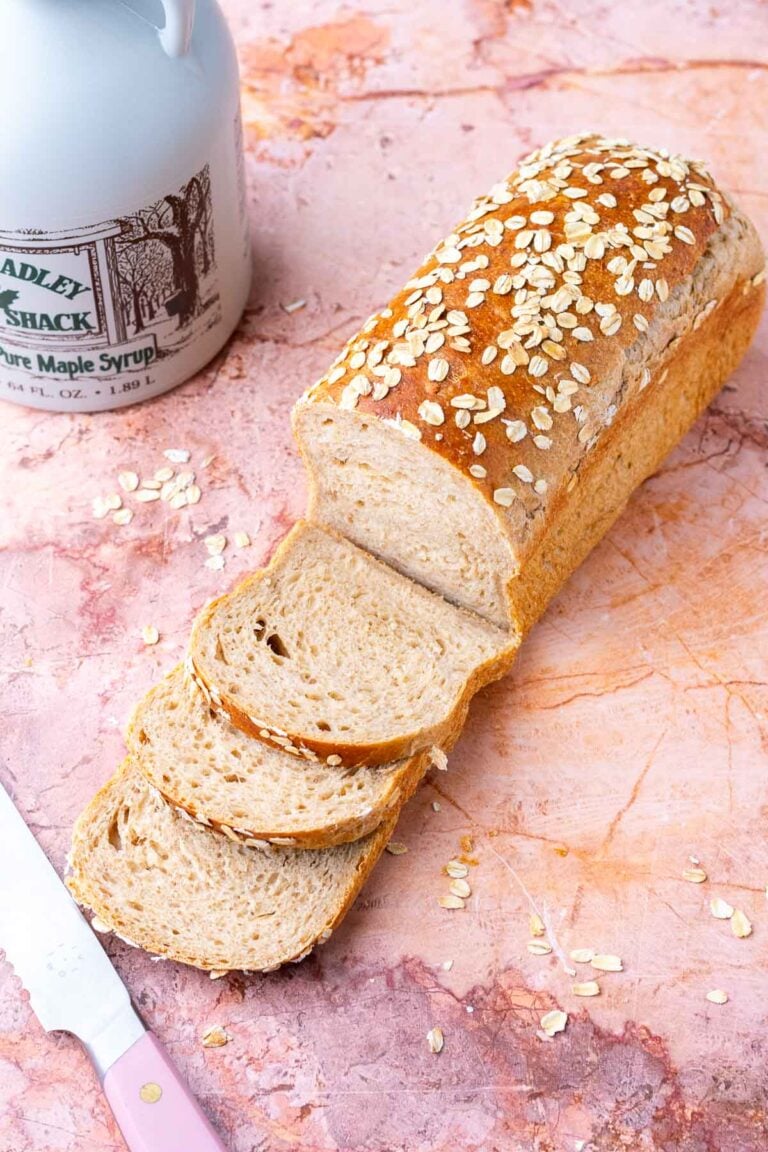 Loaf of maple oat sourdough sandwich bread with three slices and bread knife.