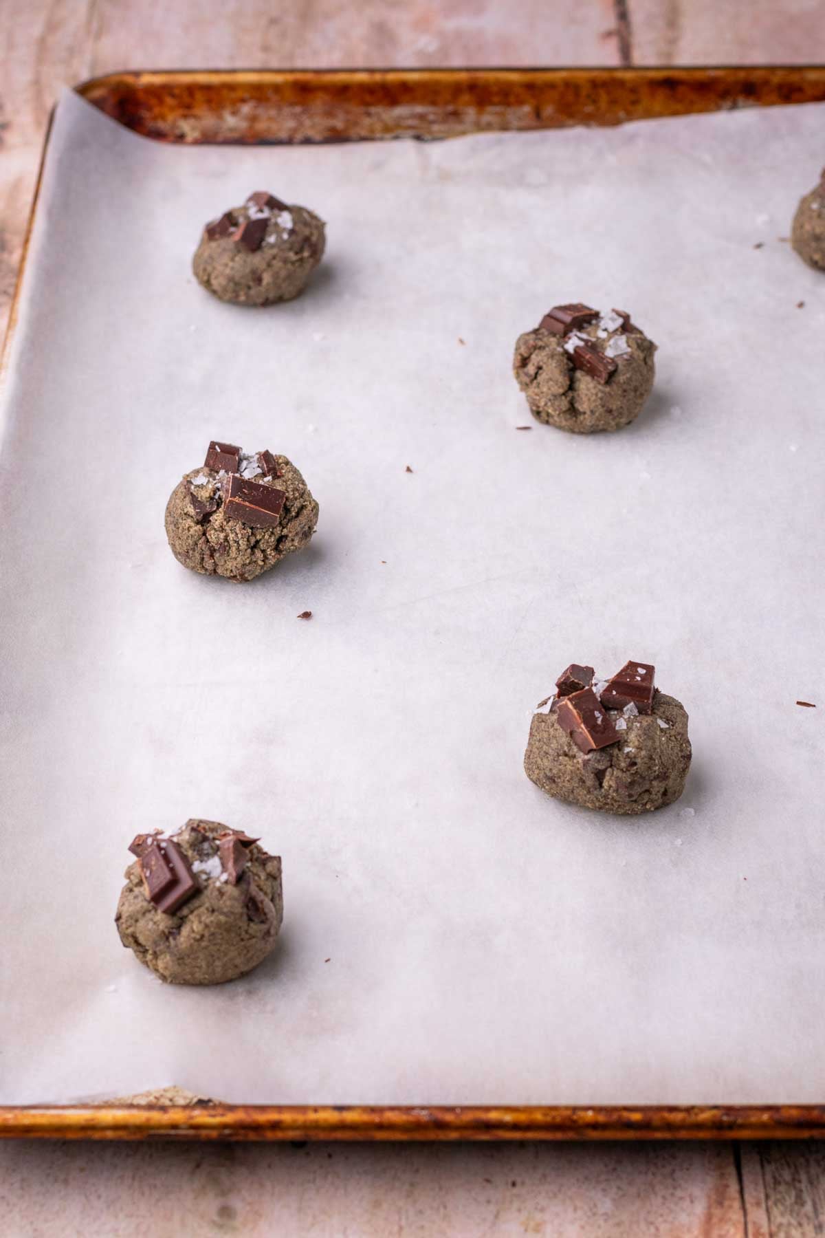 Unbaked sourdough buckwheat chocolate chip cookies on a sheet pan with parchment paper.