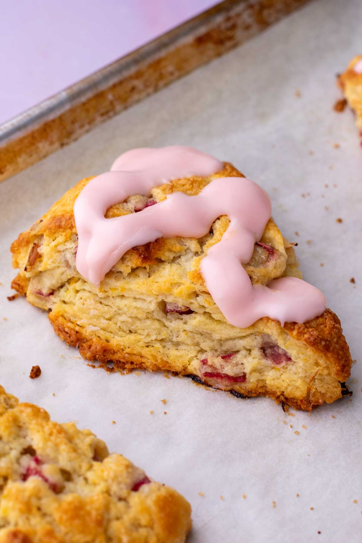 Baked sourdough rhubarb scone with Campari orange glaze on a parchment lined baking sheet.