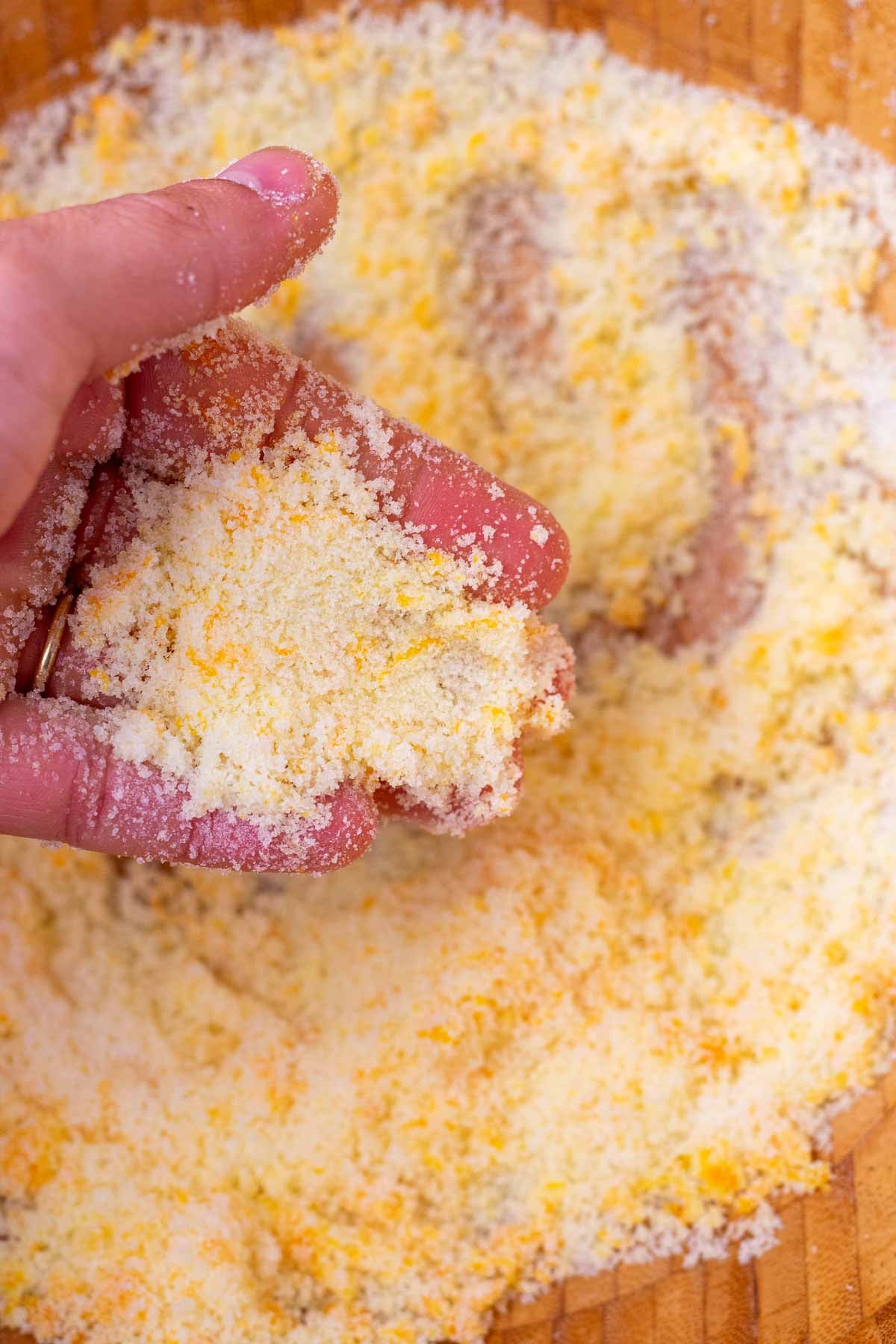 Hand rubbing orange zest into a large bowl of sugar.