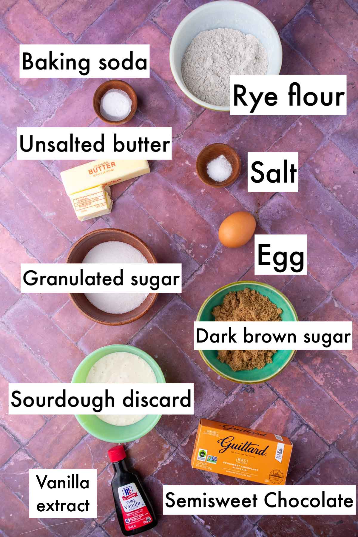 Labeled bowls of ingredients needed for sourdough rye chocolate chip cookie including baking soda, rye flour, unsalted butter, salt, egg, granulated sugar, dark brown sugar, sourdough discard, semisweet chocolate, and vanilla extract.