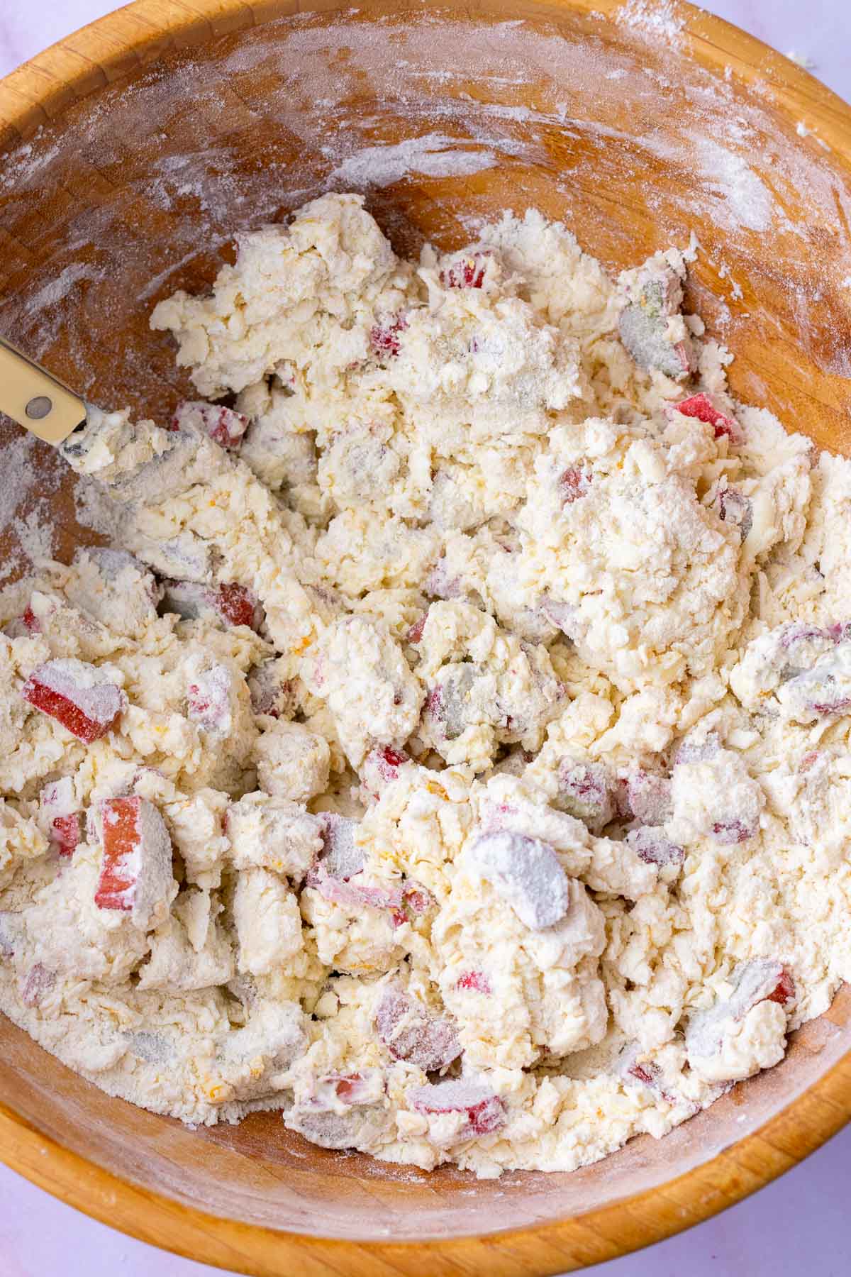 Mixing sourdough rhubarb scones dough in a large wooden bowl with a fork forming clumps.