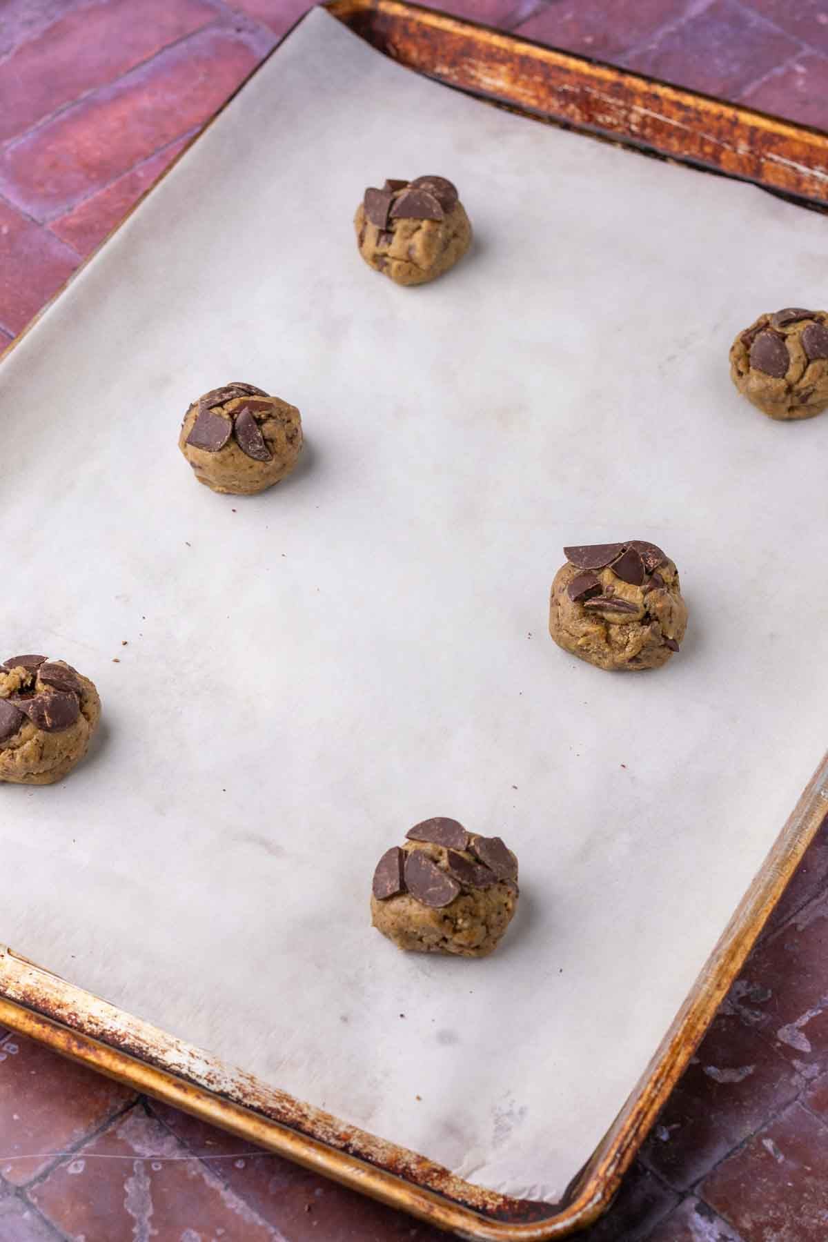 Six sourdough rye chocolate chip cookie balls on a sheet pan with parchment paper before baking.