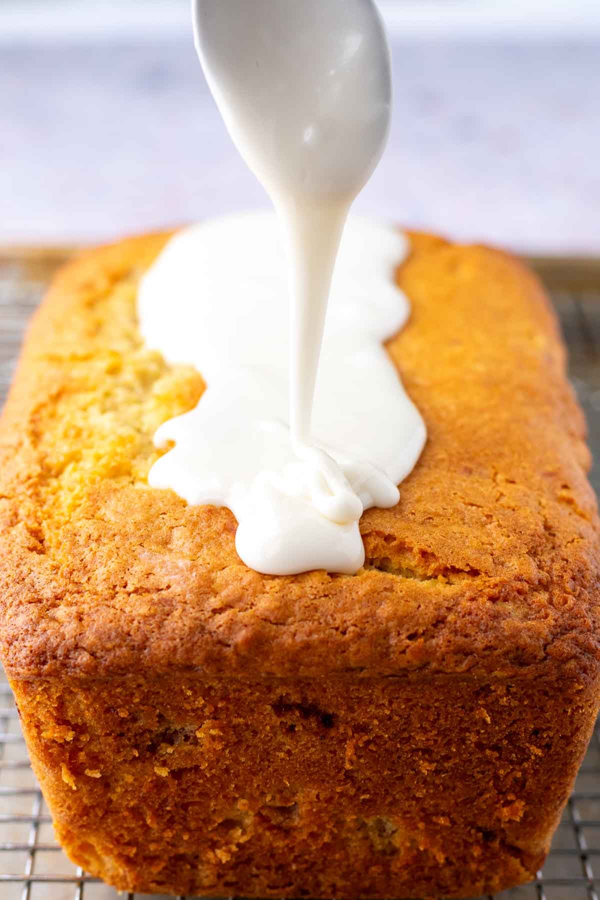 Drizzling vanilla glaze on Sourdough Strawberry Bread with a spoon.