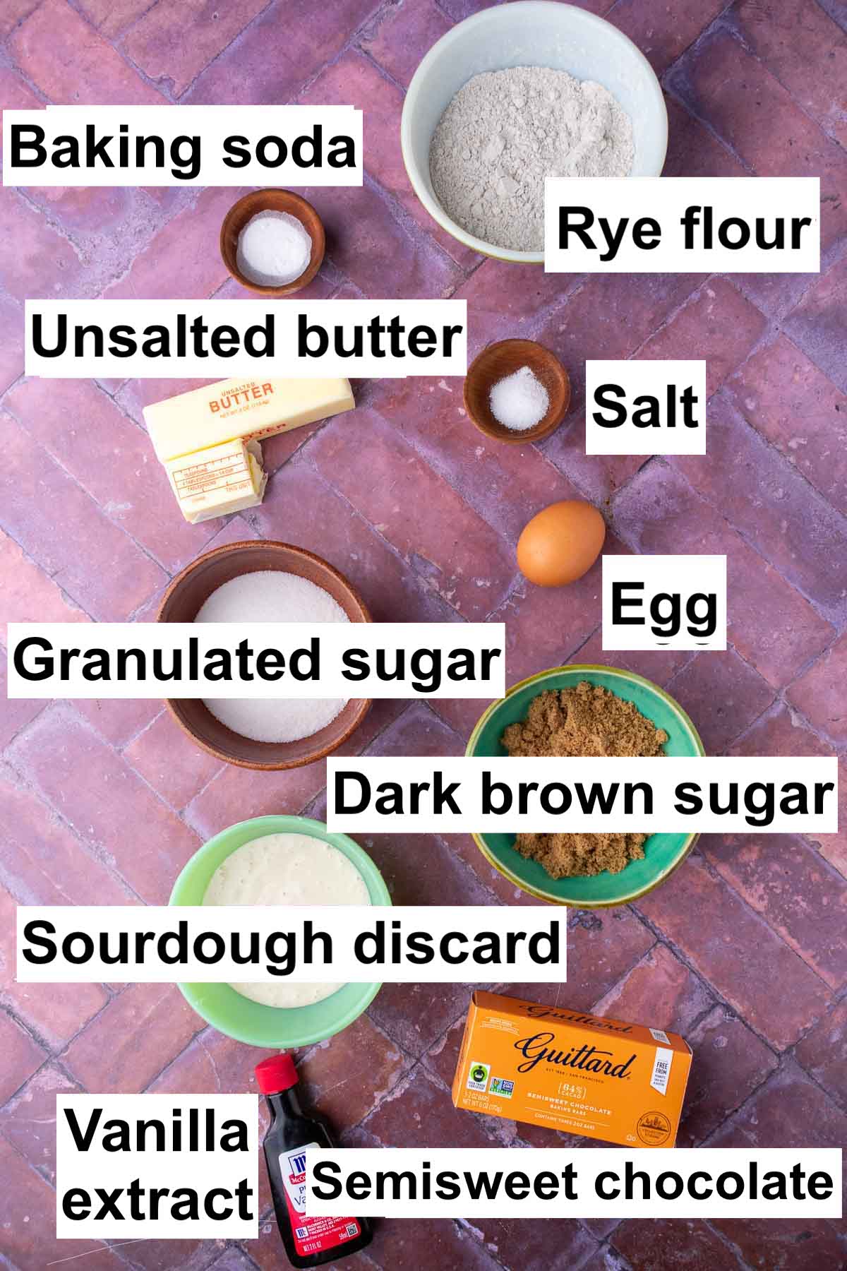 Labeled bowls of ingredients needed for sourdough rye chocolate chip cookie including baking soda, rye flour, unsalted butter, salt, egg, granulated sugar, dark brown sugar, sourdough discard, semisweet chocolate, and vanilla extract.